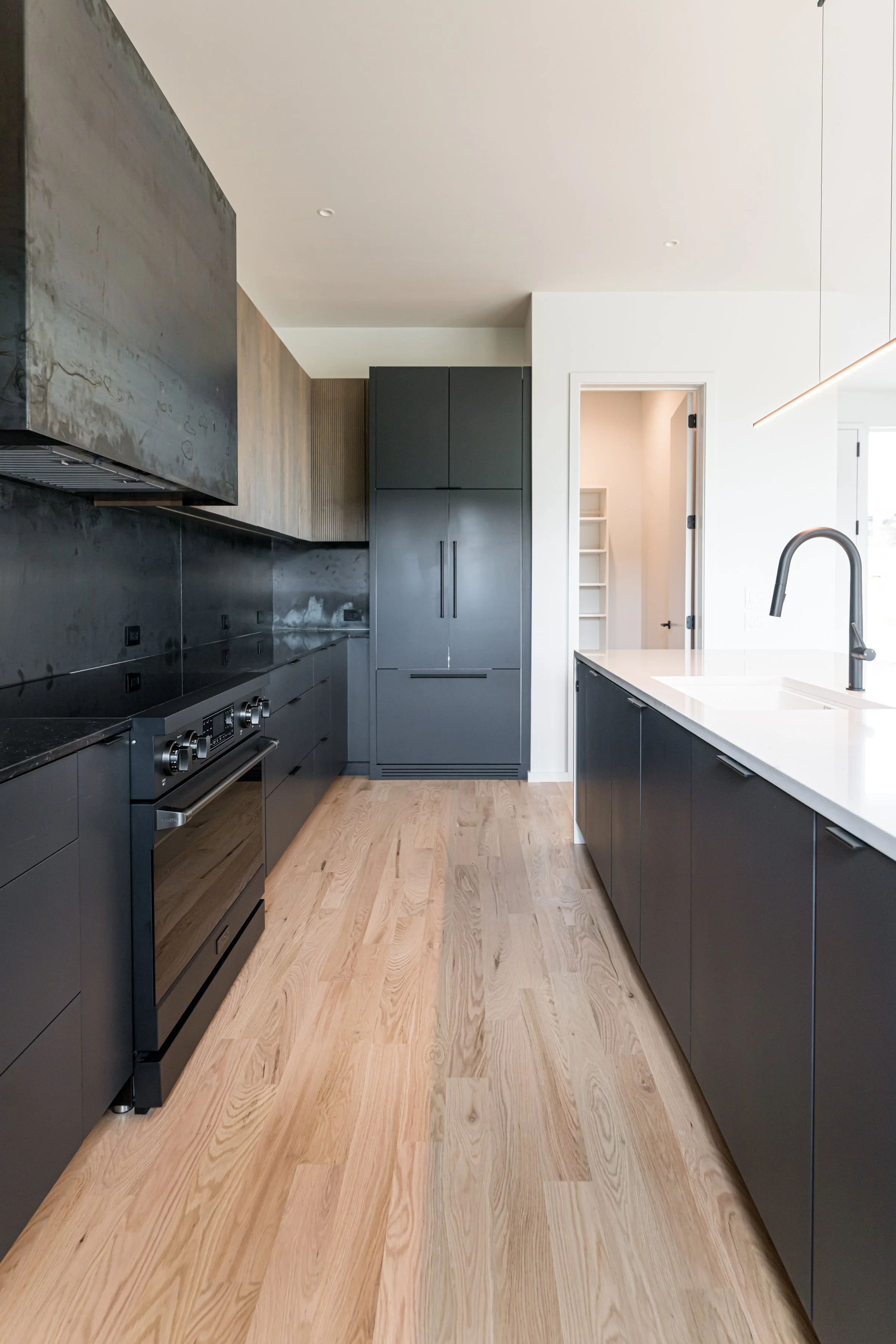 Modern kitchen with black cabinetry, light wooden flooring, white countertop, and a black faucet.