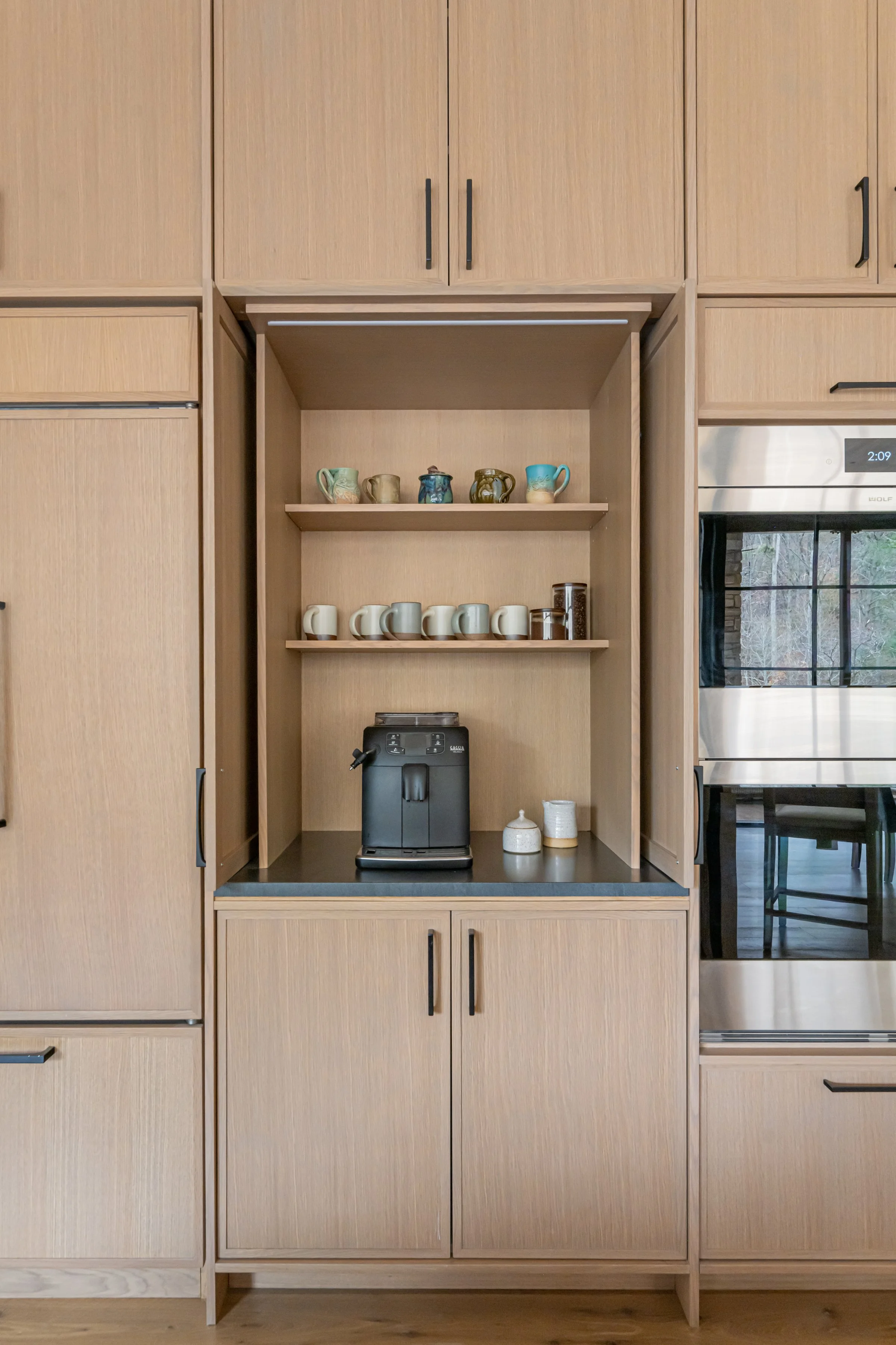 Kitchen cabinet with open shelves holding coffee mugs, teapots, and a coffee machine.