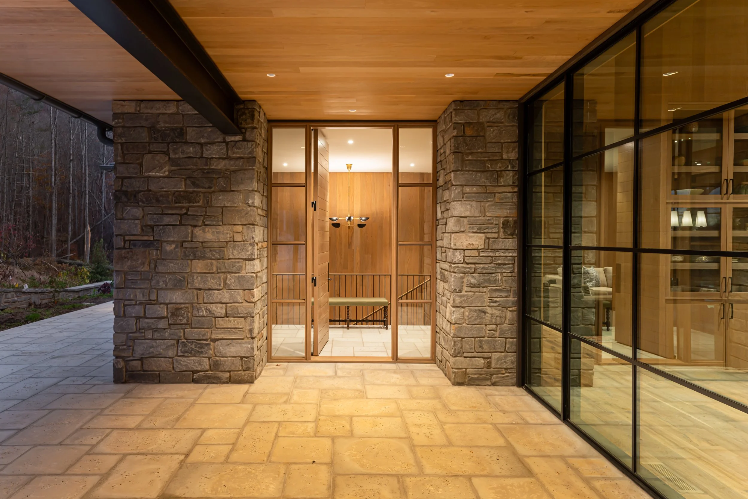 View of an exterior porch area leading to an interior hallway with stone columns, wooden ceiling, and glass sliding doors.