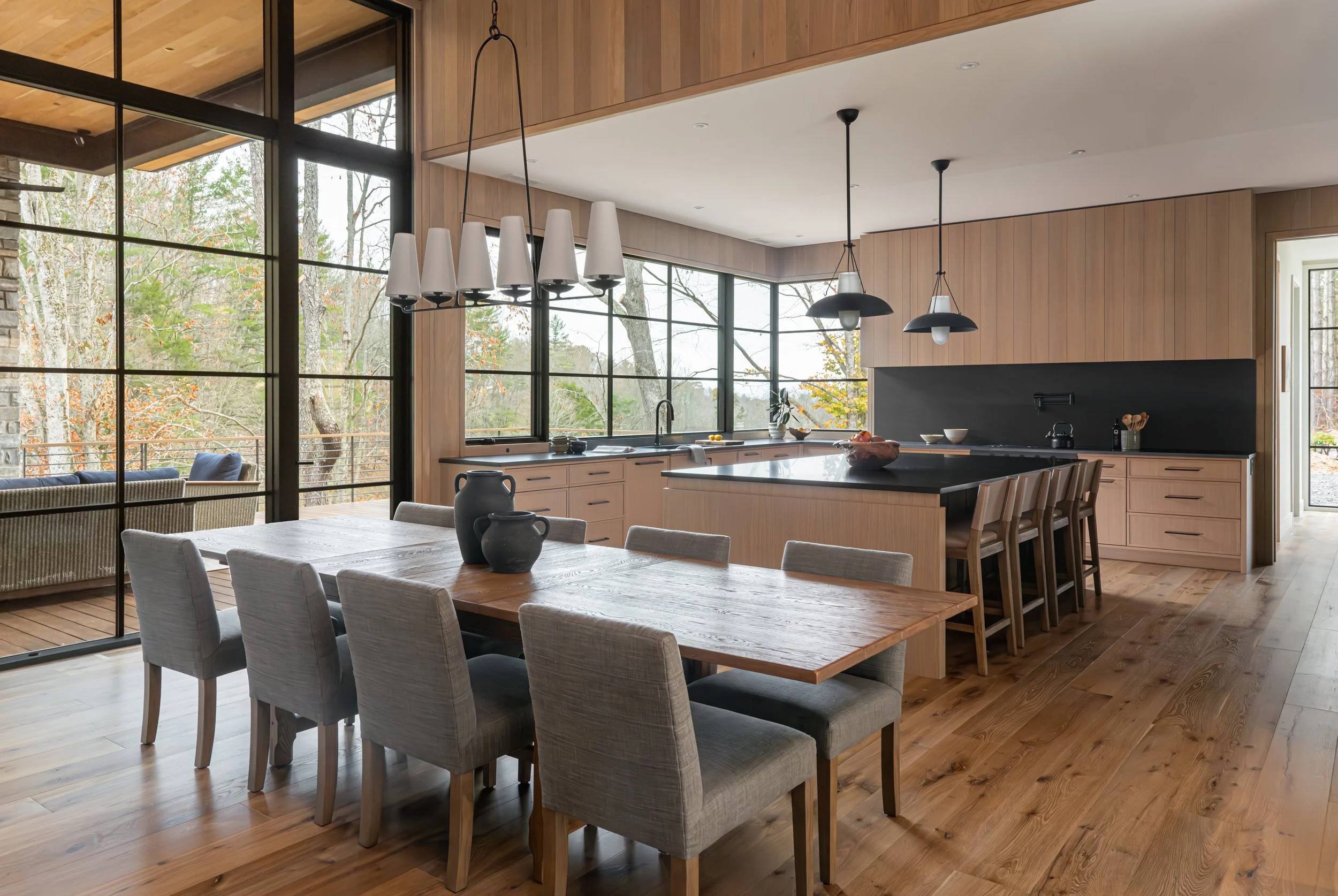 Modern open-concept kitchen and dining area with large windows, wooden floors, and minimalist decor.