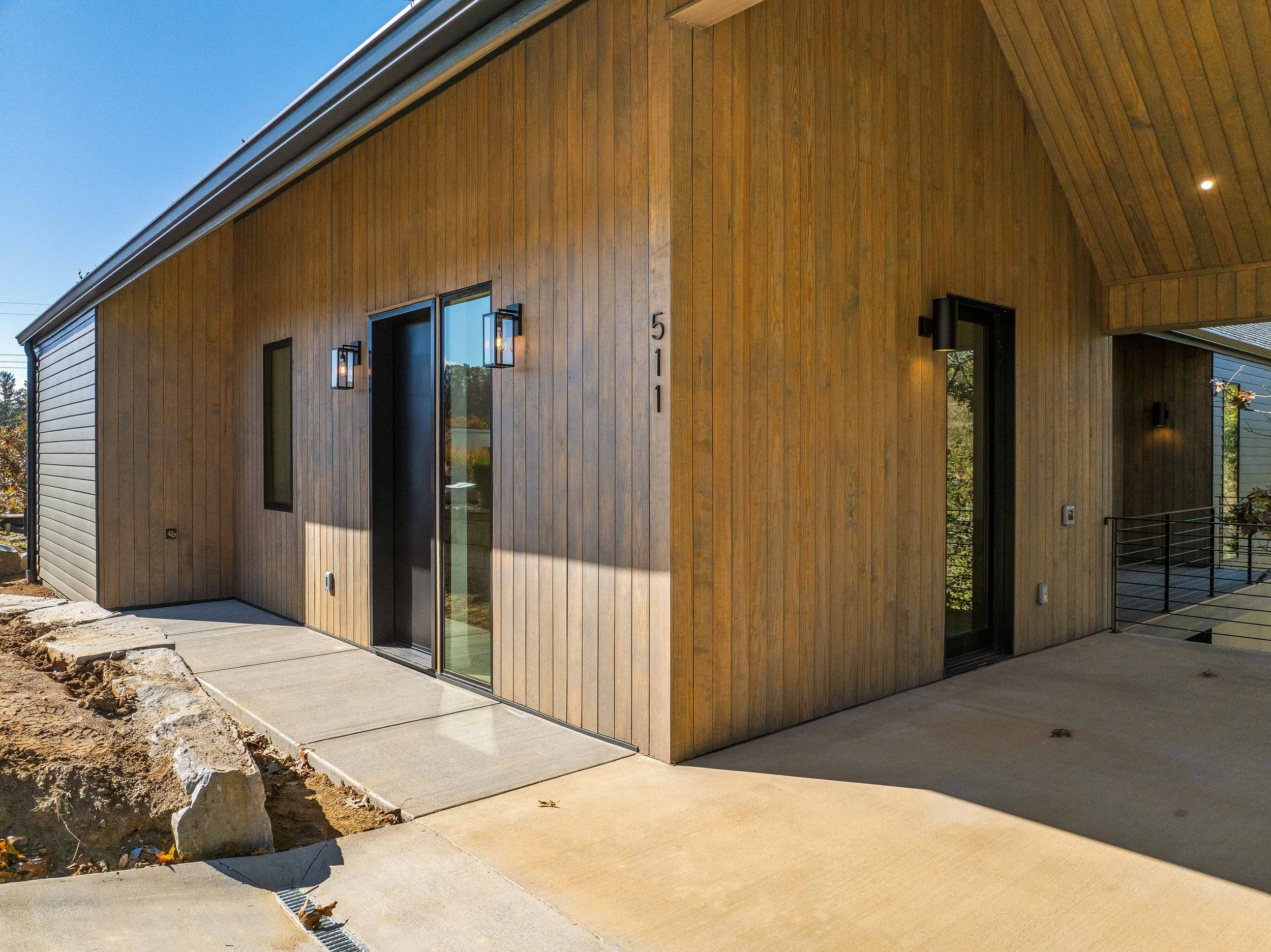 Modern house exterior with wooden siding, black doors, and wall-mounted lights, numbered 511, at a sunny outdoor setting