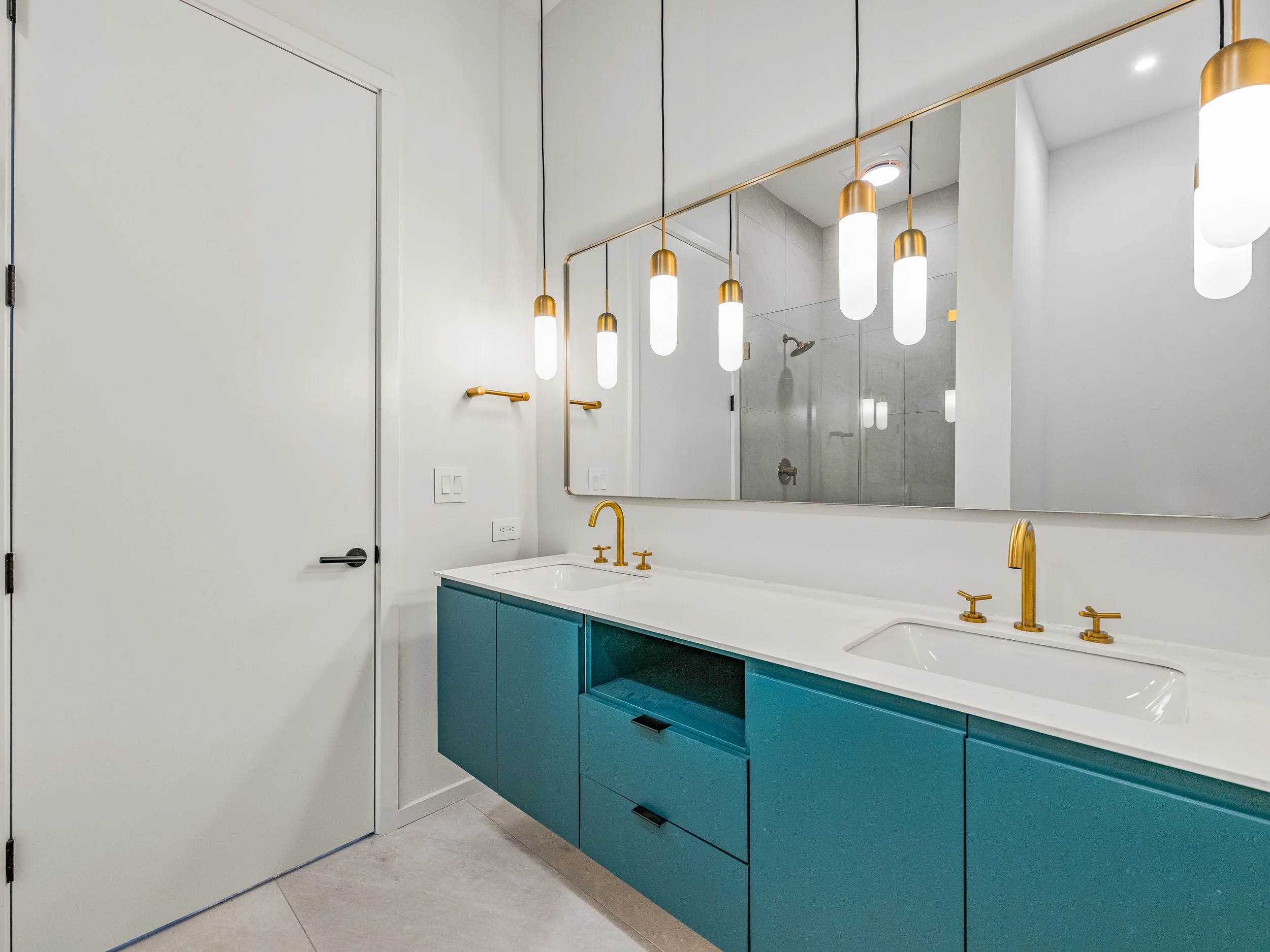 Modern bathroom with white walls, a large mirror, blue vanity with gold fixtures, and pendant lights.