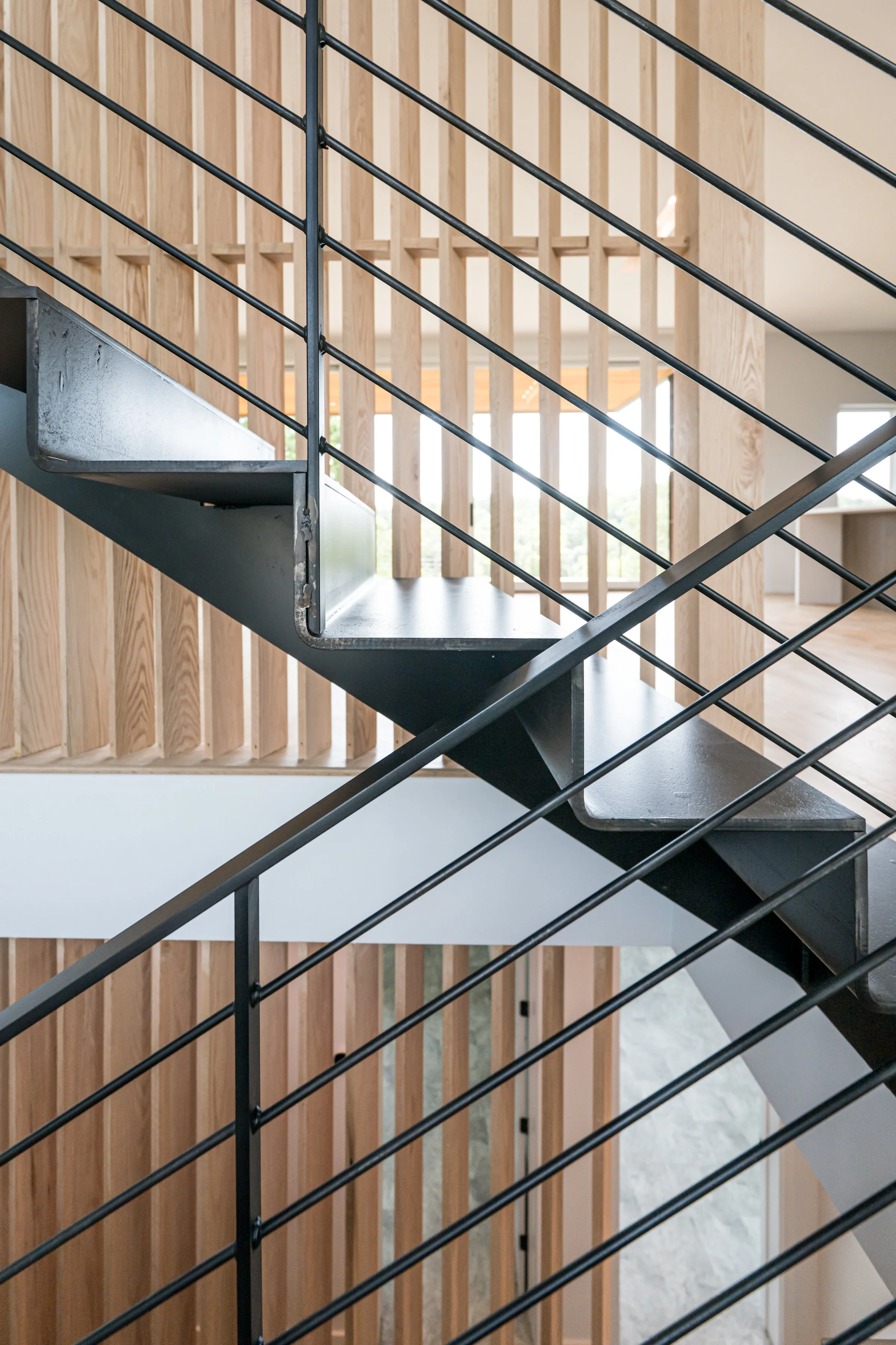 Interior view of a modern staircase with black metal handrail and wooden vertical slats in the background.