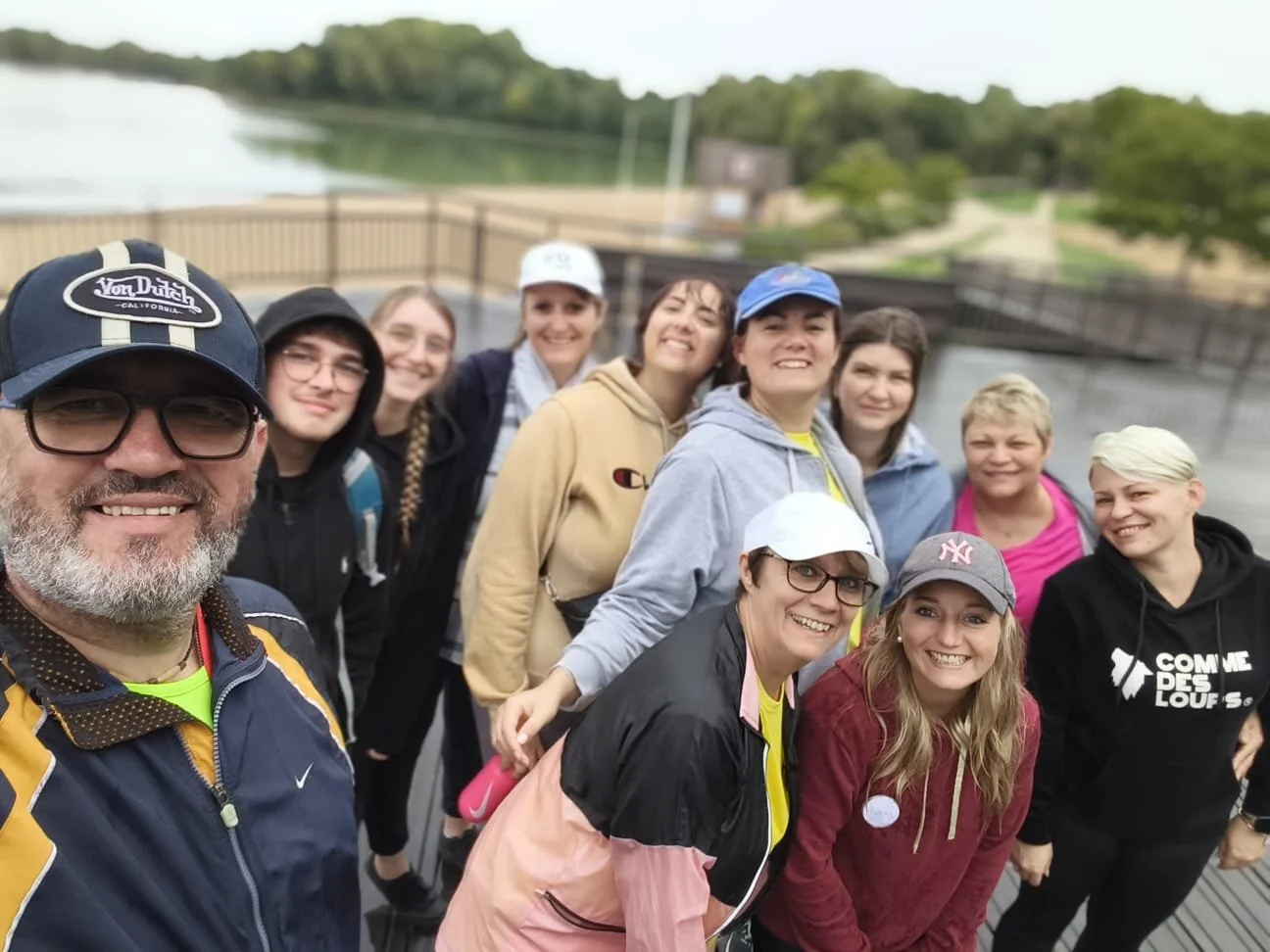 Un groupe de personnes souriantes posant pour une photo en extérieur près d'une rivière, avec un pont en arrière-plan.