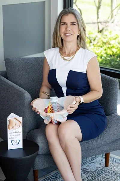 Christine LaM'ee sitting in a chair, holding an anatomic model of a pelvis.