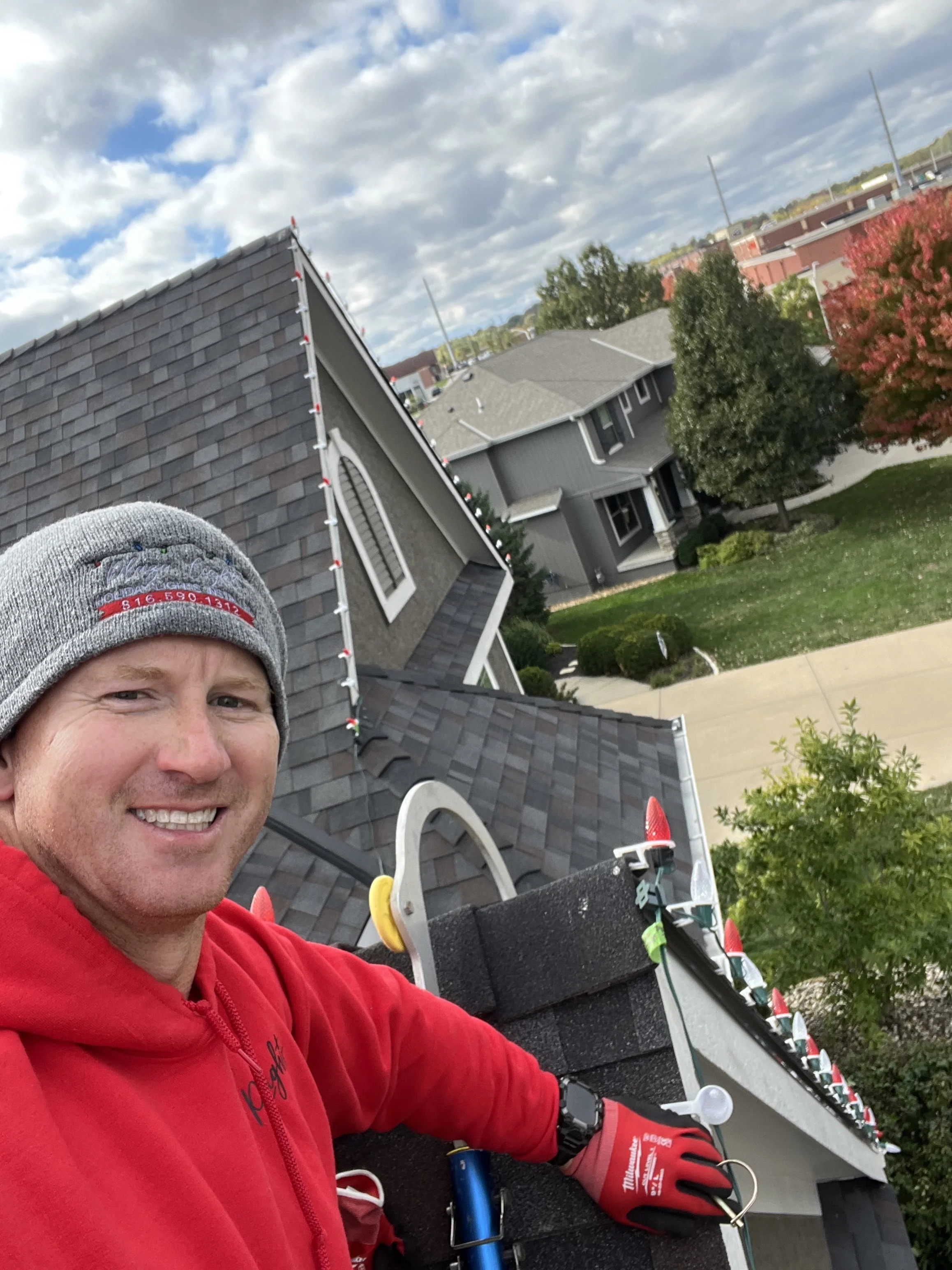 Plaza Lights House installation of lights, installer on roof using safety ladder clipping on c9 warm white and red lights in Johnson County KS