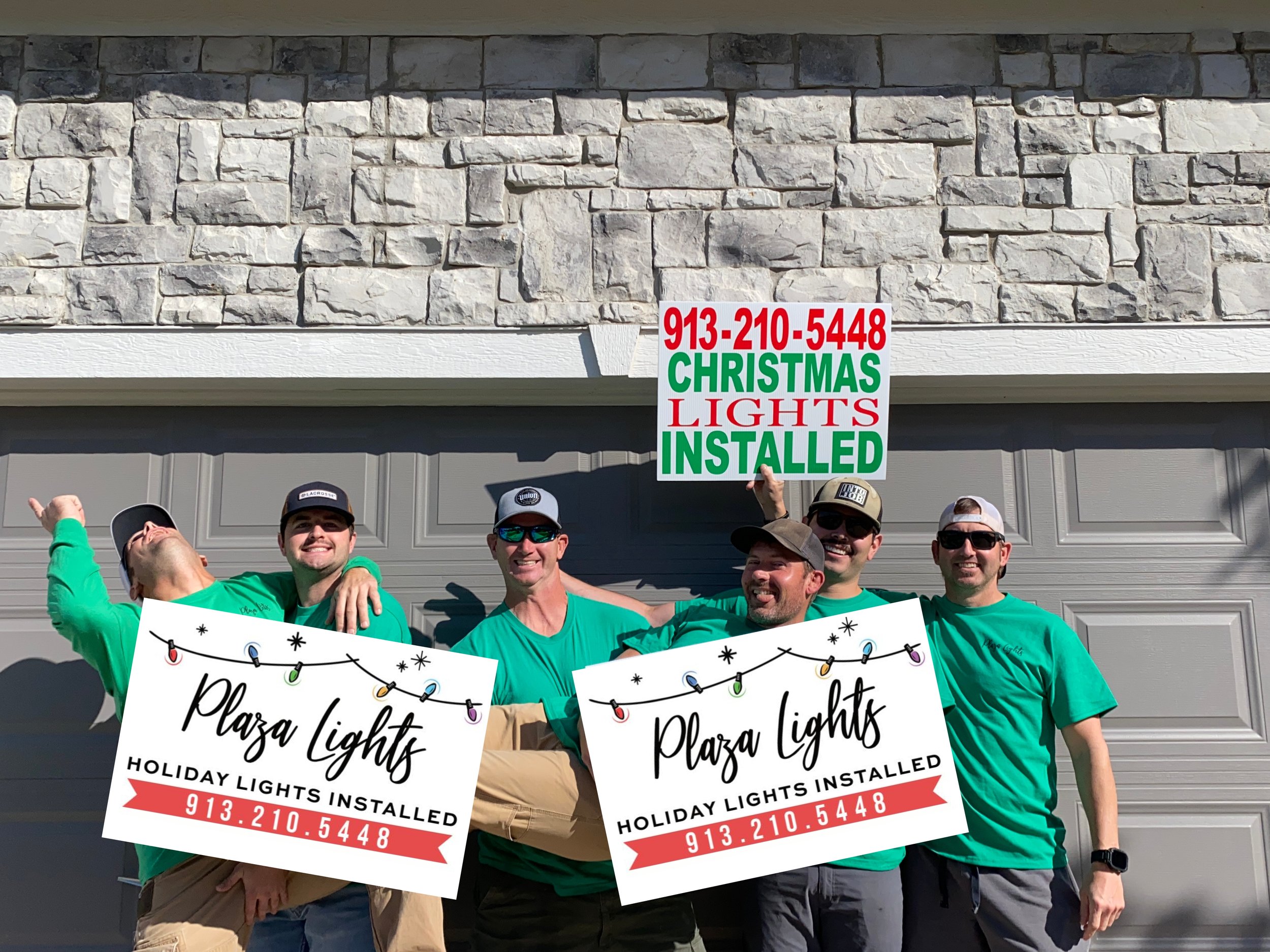 Off-duty Plaza Lights firefighter team holding Plaza Lights yard signs in front of a customer's garage