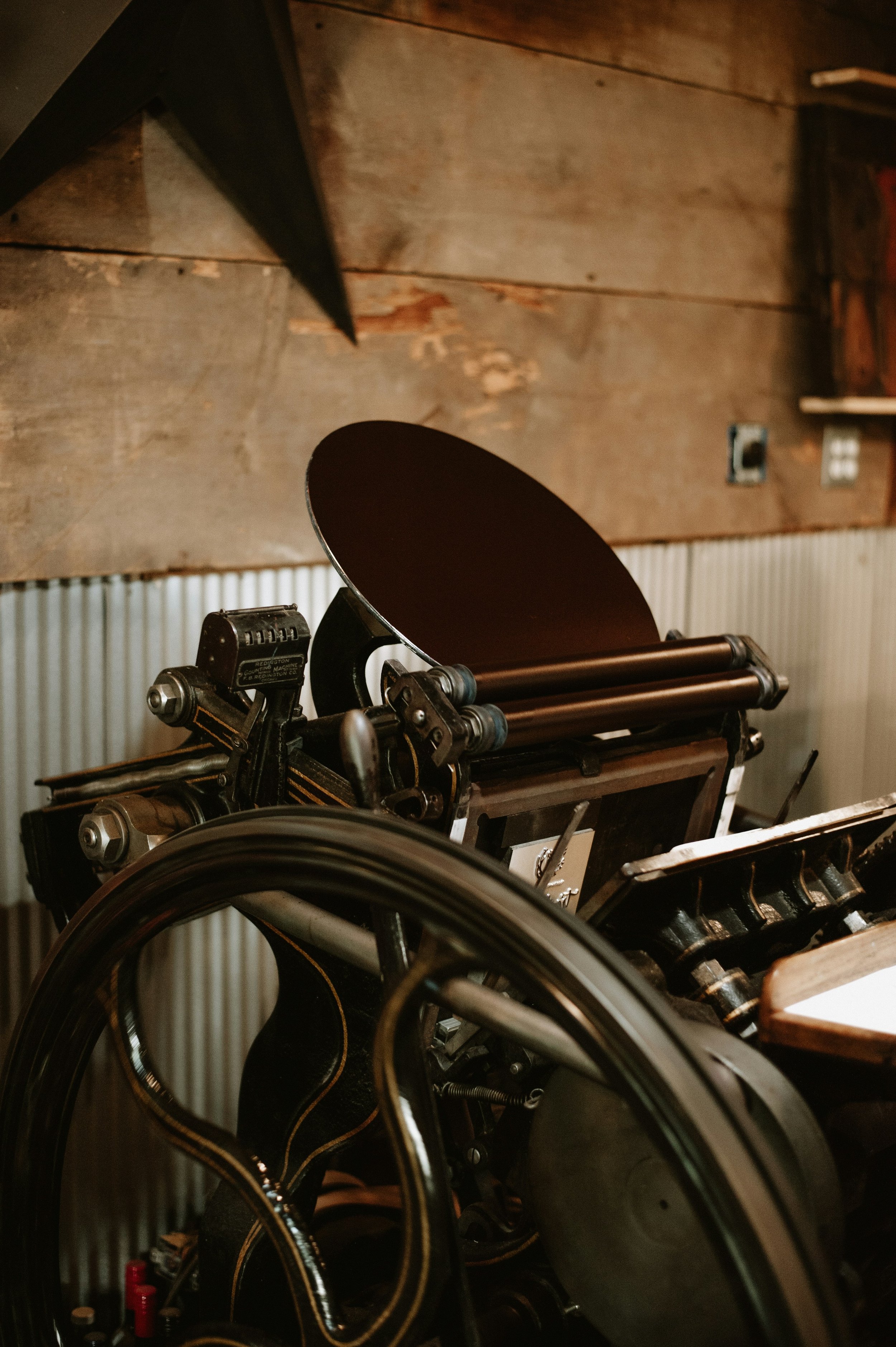Close-up of a vintage press with a large black lens and mechanical parts, positioned against a wooden wall interior.