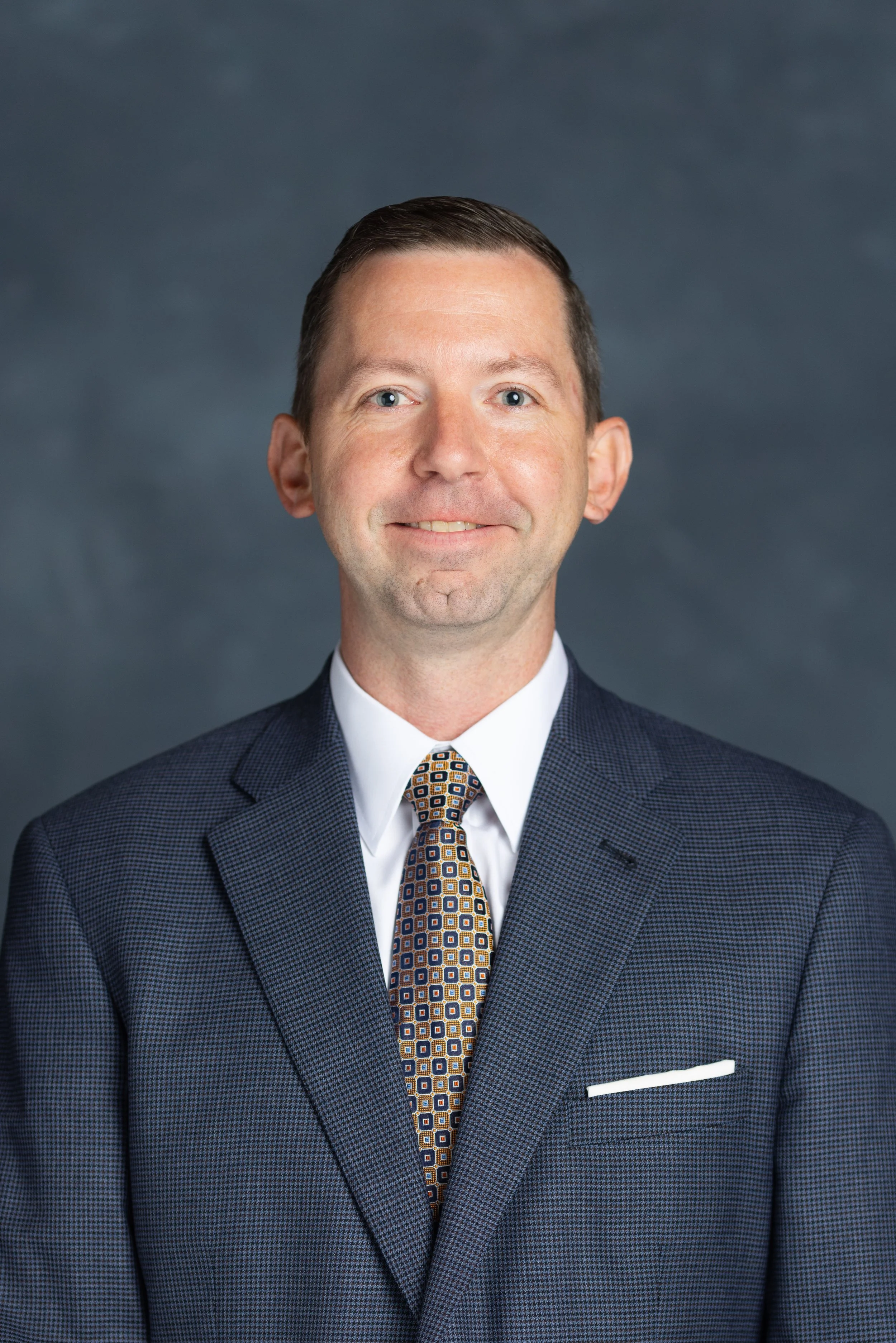 Executive corporate headshot of a man in a dark suit and patterned tie against a dark studio background, captured by Lexington KY headshot photographer 859 Photography.