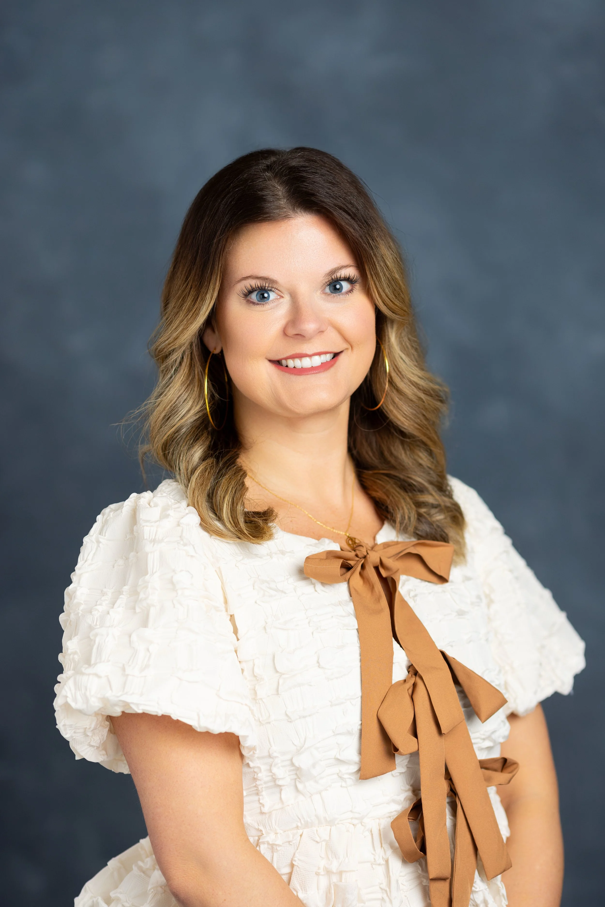 Professional lifestyle headshot of a woman in a textured white dress against a grey studio background, captured by 859 Photography in Lexington, KY.