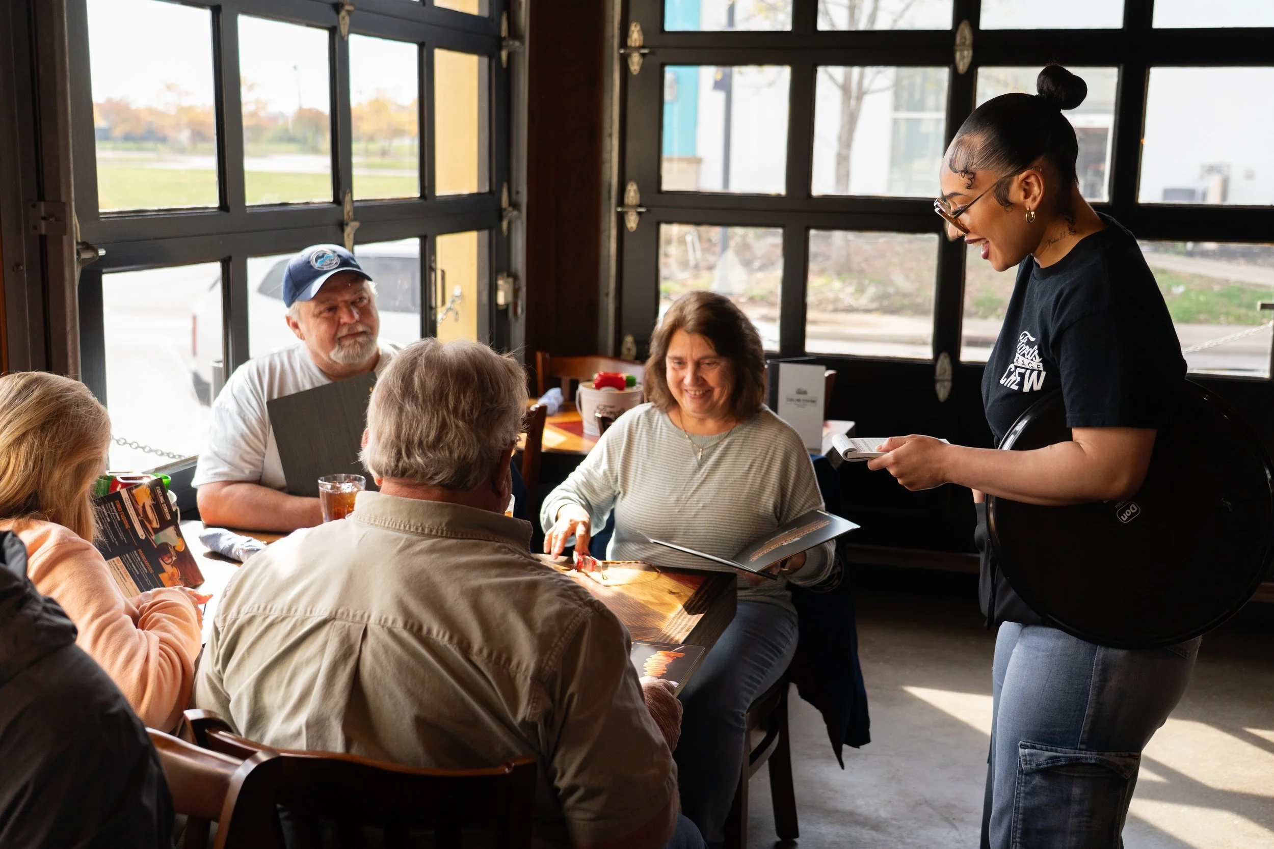 Candid dining experience and hospitality photography at Ford's Garage in Lexington, KY, featuring a server taking orders in the sunlit dining room, by 859 Photography.