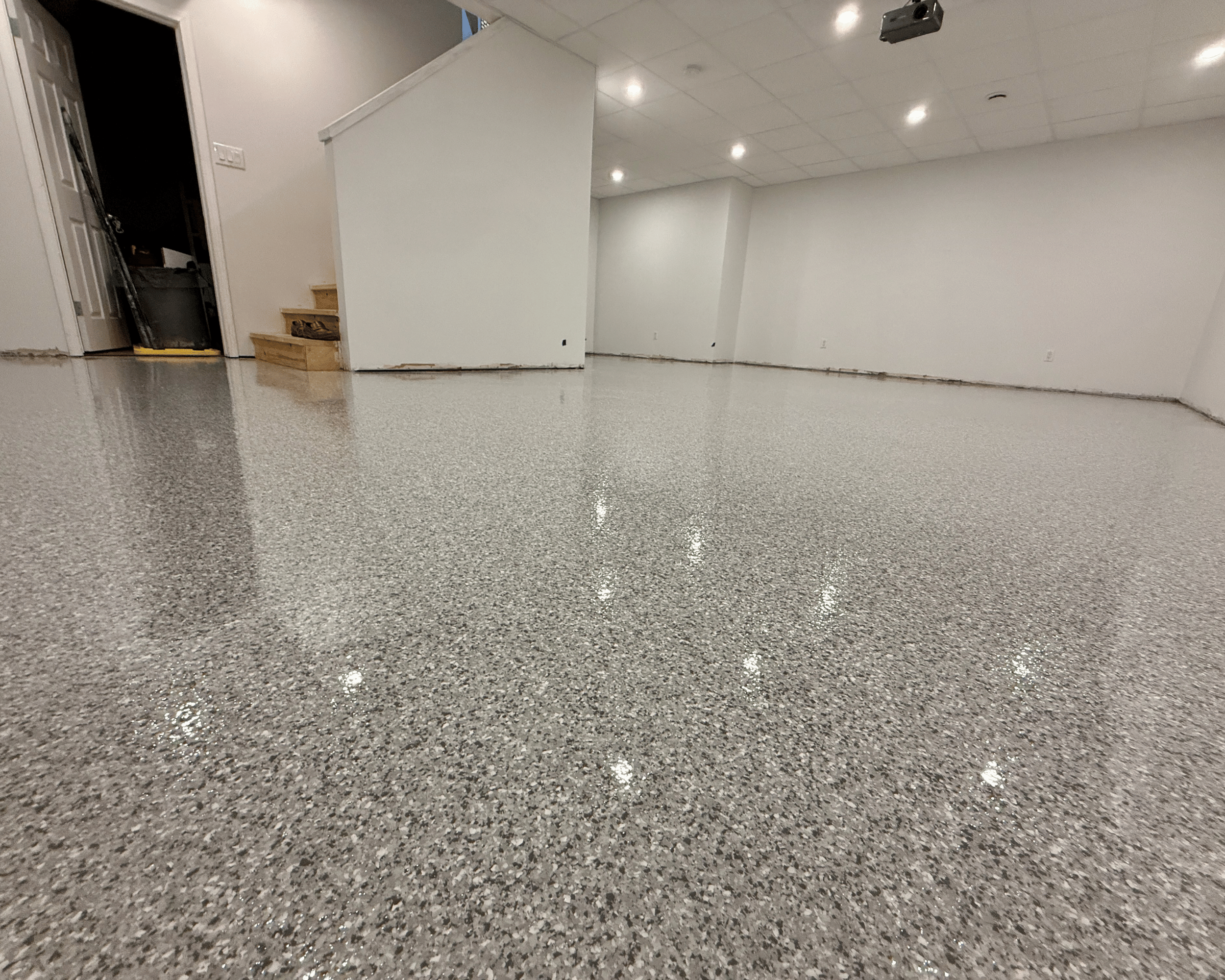 Empty room with a polished speckled gray concrete floor, white walls, and a white ceiling with embedded lights.