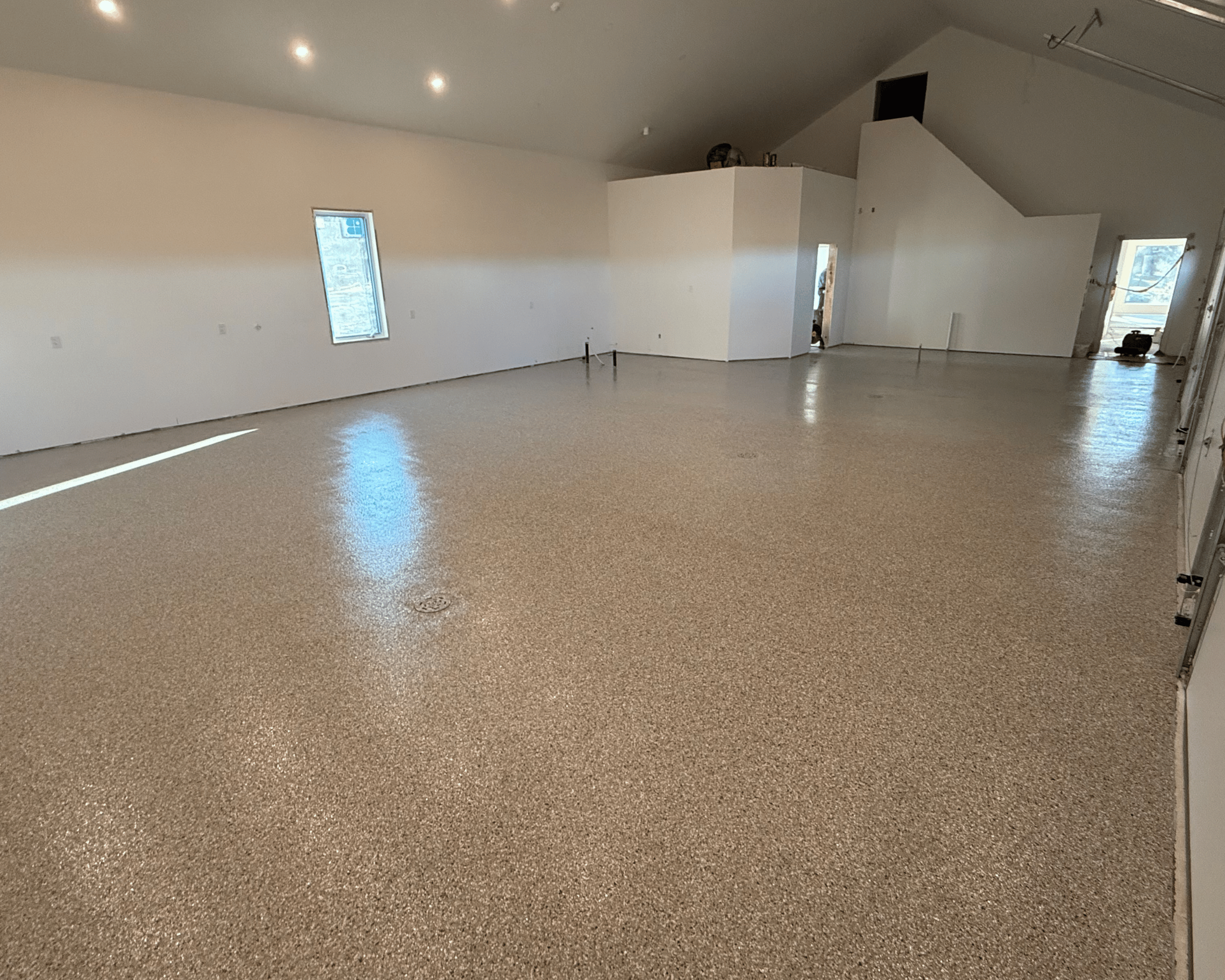 Empty, spacious room with new flooring, white walls, small windows, and recessed lighting on ceiling, likely under construction or renovation.