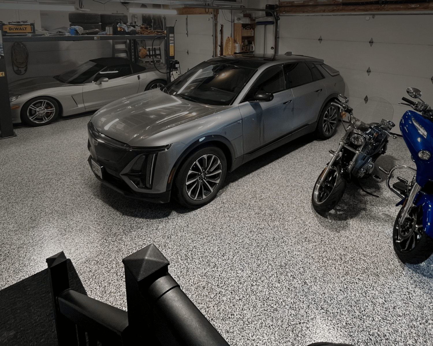 A garage containing a gray electric SUV, a silver sports car, and two motorcycles.