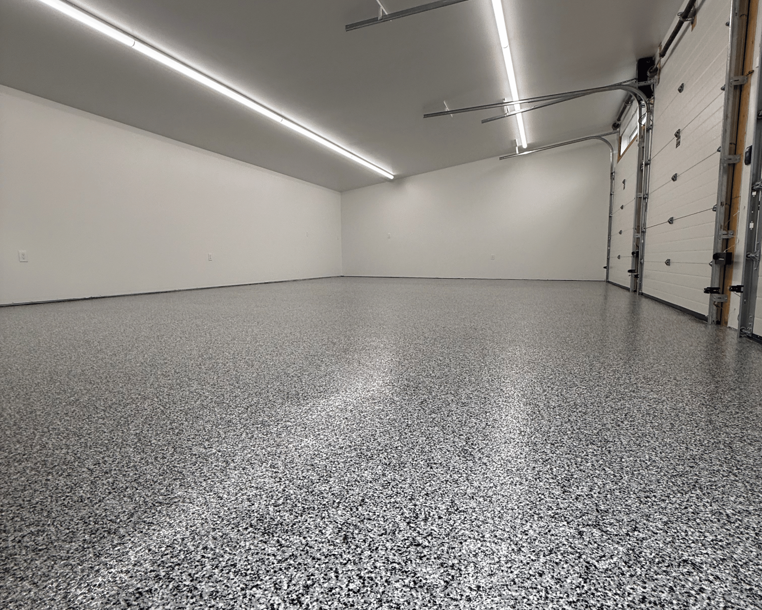 Empty clean garage with speckled gray epoxy floor, white walls, and open garage doors with metal tracks.