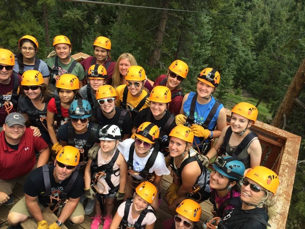 Group of people wearing helmets and harnesses on a forested outdoor adventure.