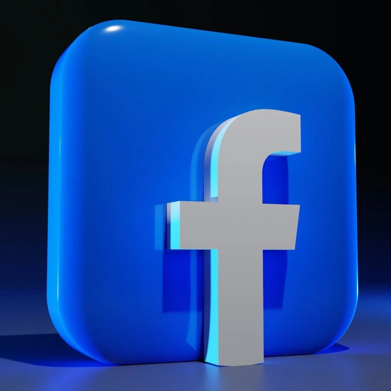 A blue 3D Facebook logo with a white lowercase 'f' in the center, illuminated against a dark background.