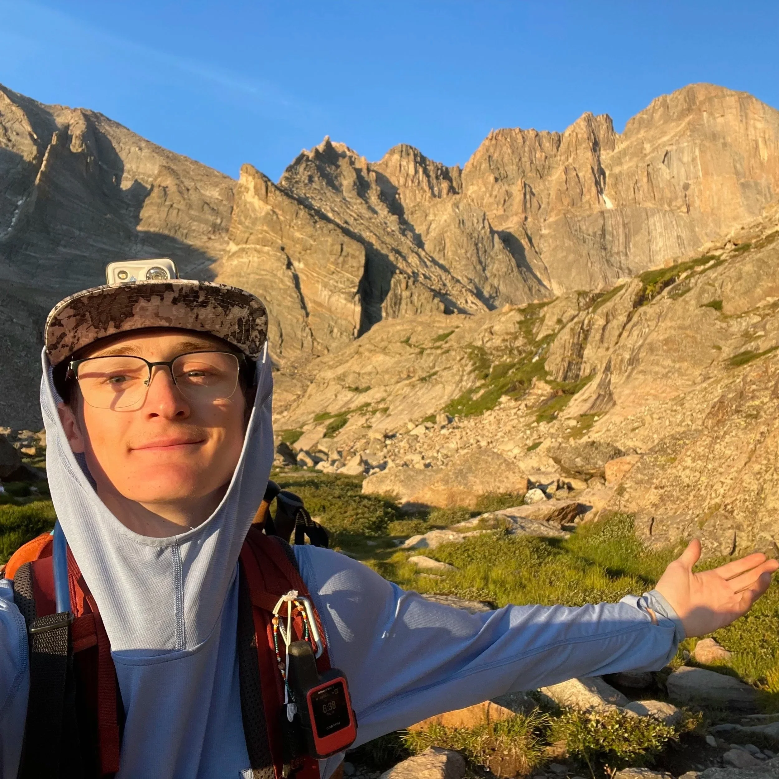 Young man taking a selfie outdoors in a mountainous area with rocky cliffs and green vegetation during daytime.