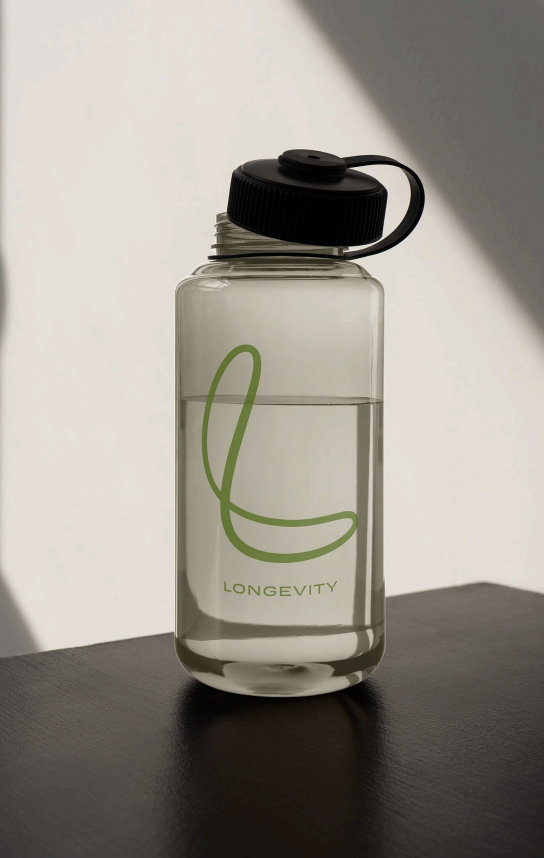 A clear water bottle with a black lid and a built-in straw, labeled with a green logo and the word "Longevity." The bottle is placed on a dark surface with a white background and a shadow.
