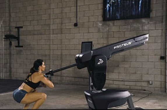 Woman exercising with a large, high-tech rowing machine in a gym.