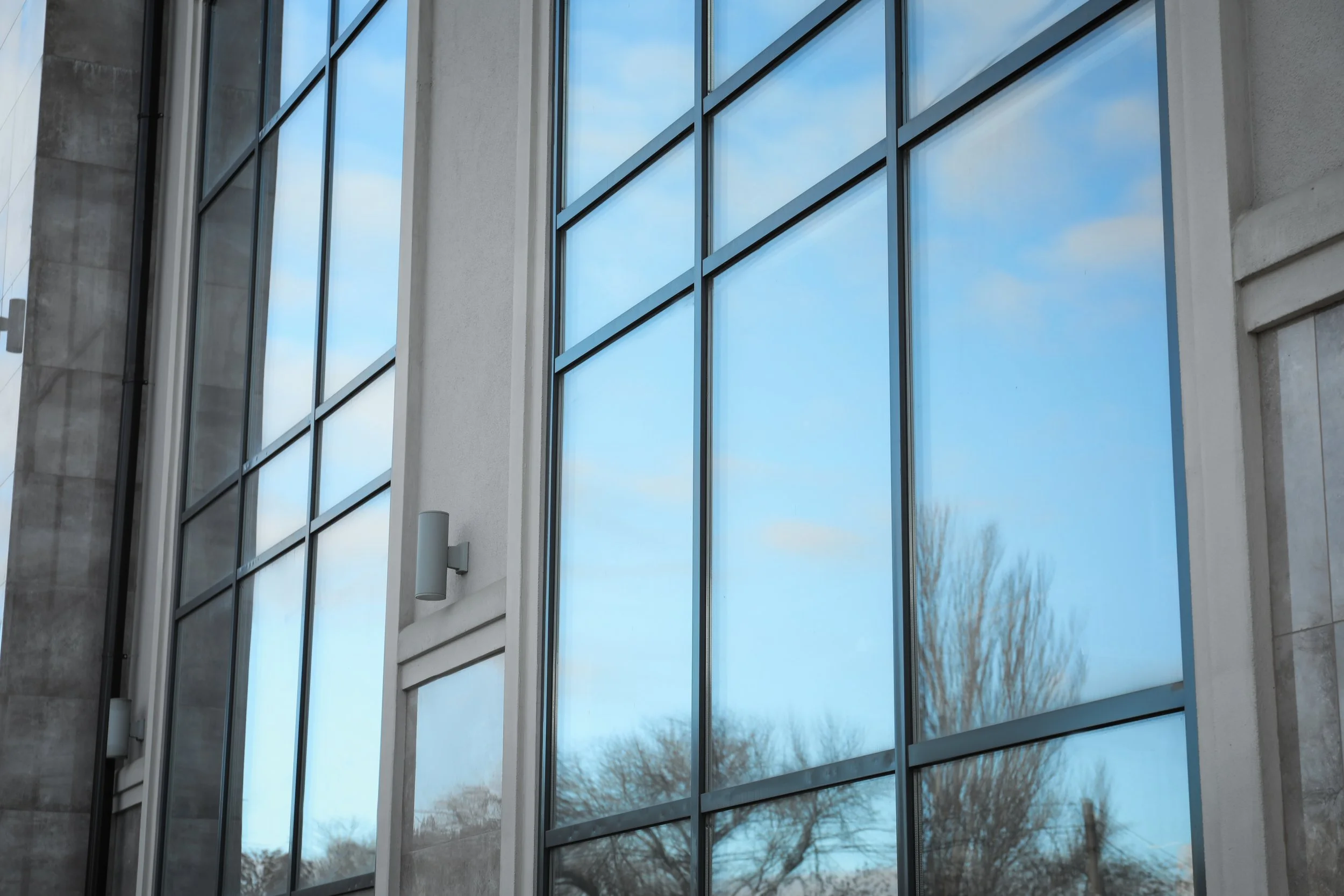 Close-up of building exterior with large reflective glass windows reflecting blue sky and trees