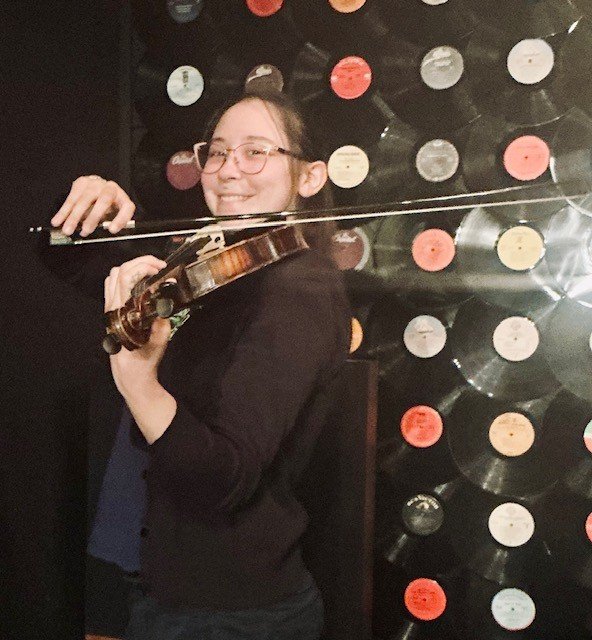 Naomi Martinez playing violin in front of a backdrop of vinyl records.