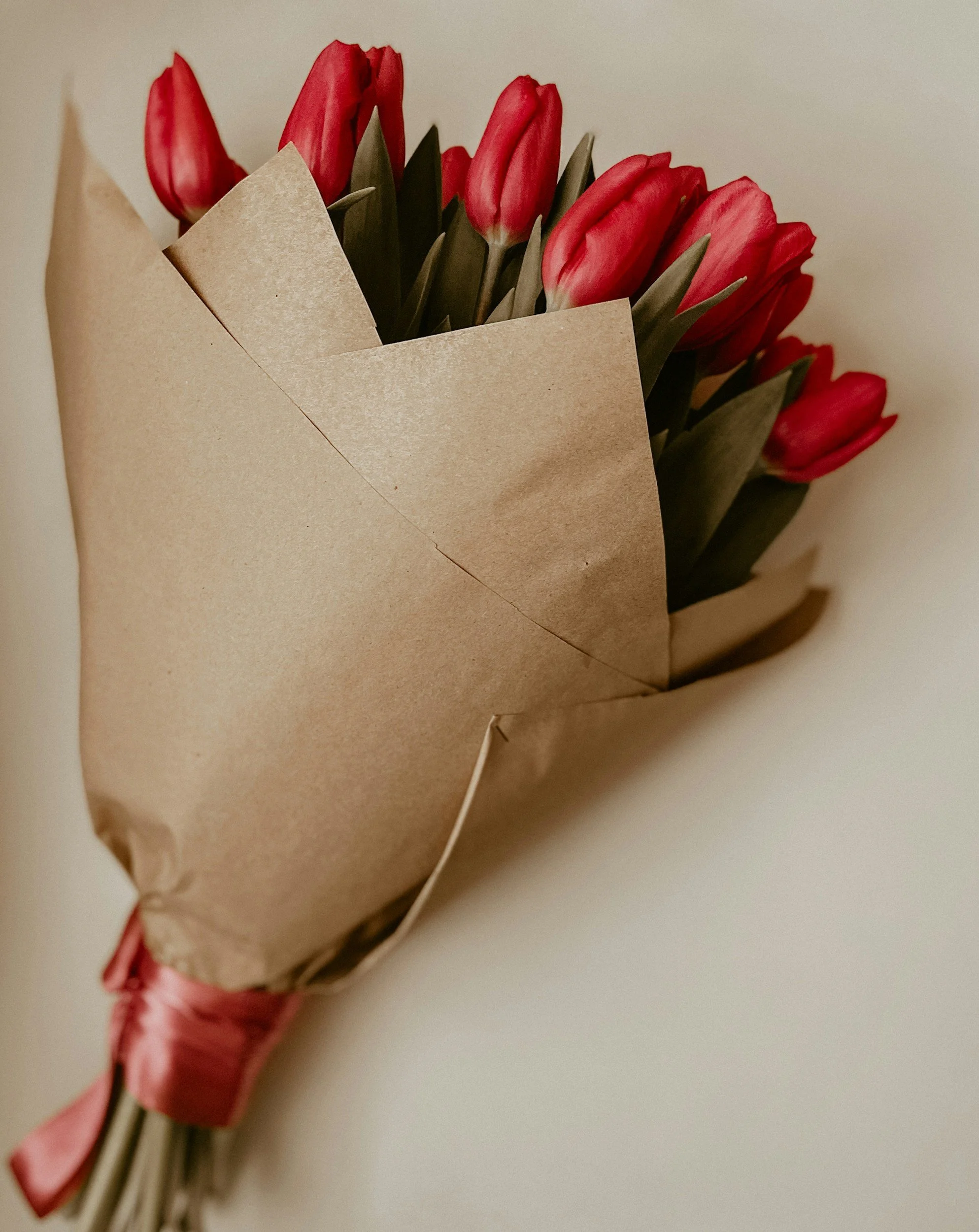 Bouquet of red tulips wrapped in brown paper, tied with a pink ribbon.