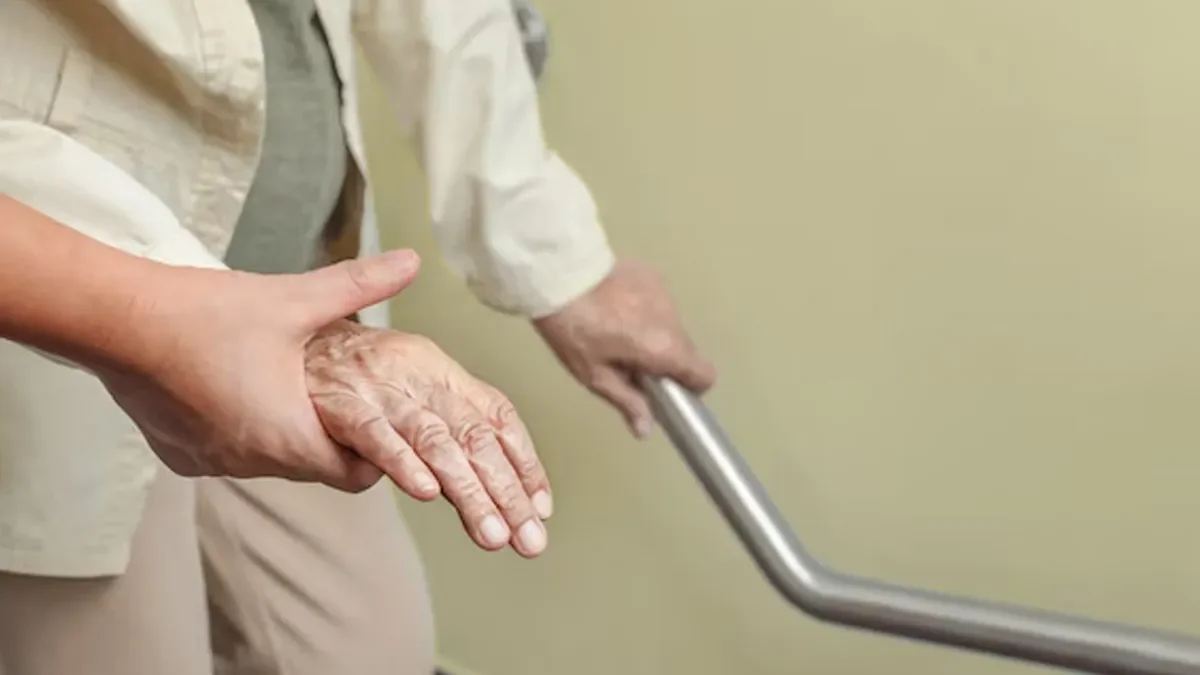 A caregiver helping an elderly person walk with a cane, supporting their hand.