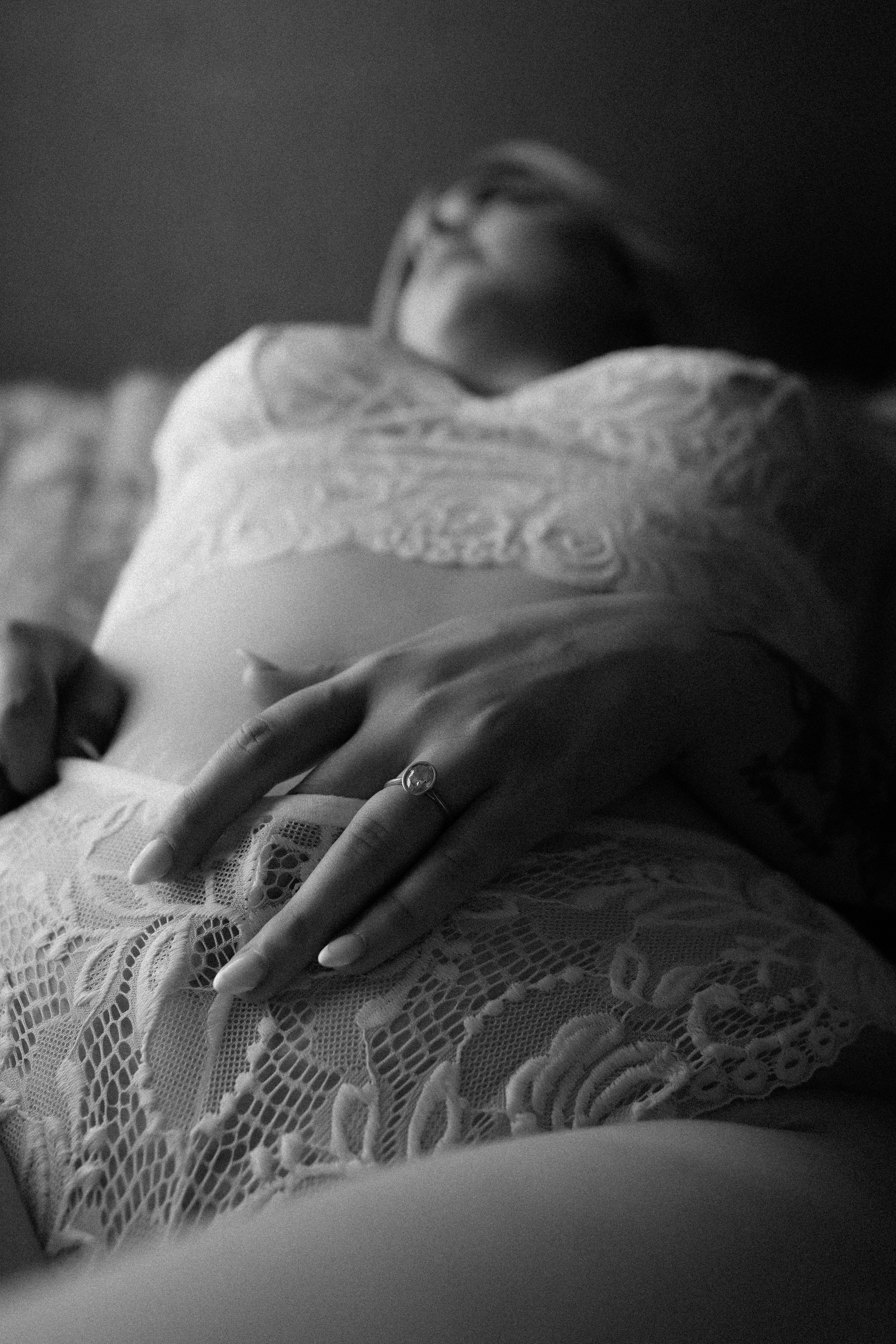Close-up of a woman lying down on her back, wearing lace clothing, with her hand resting on her stomach and a ring on her finger.