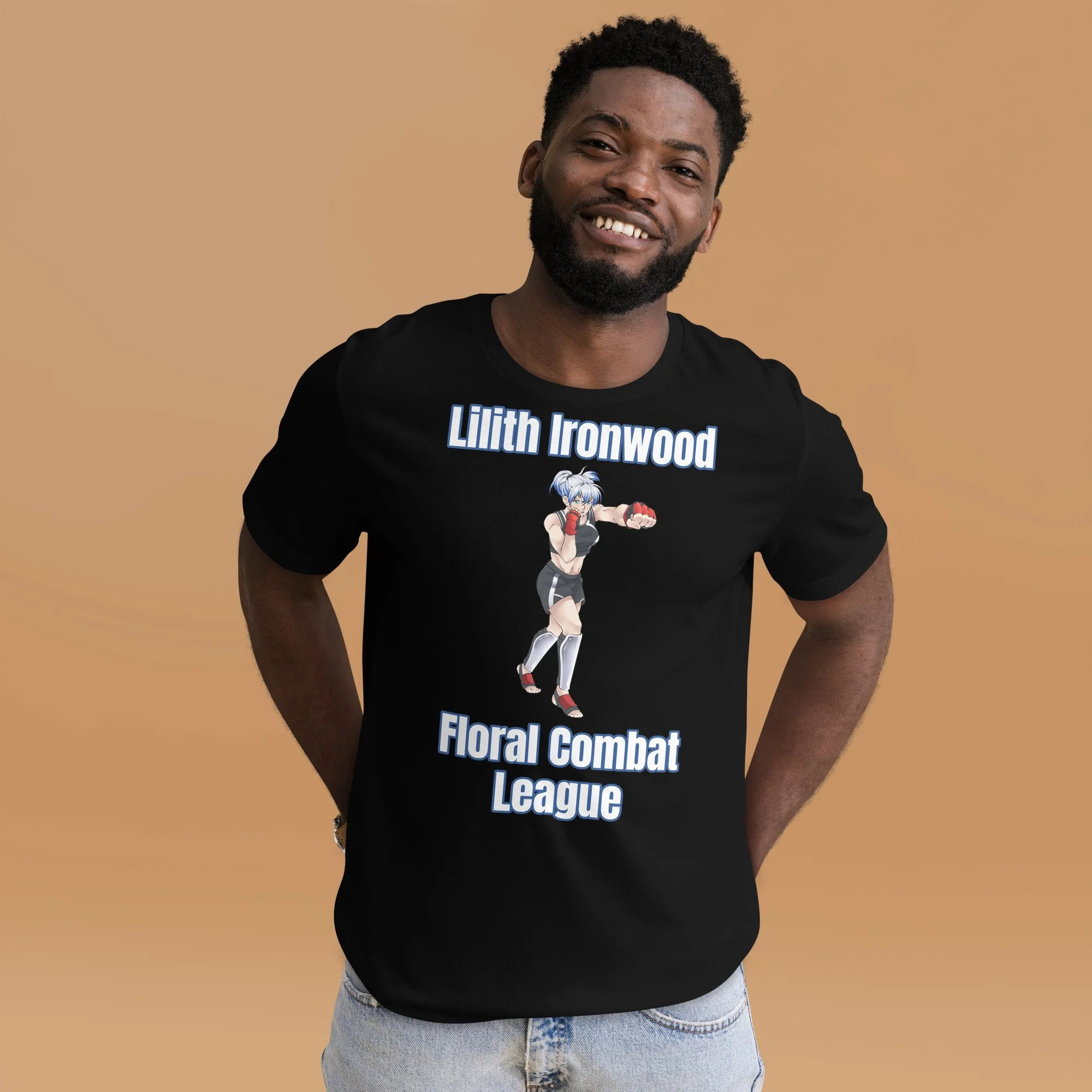 A young man with dark curly hair, a beard, and a big smile wearing a black T-shirt with a graphic of an anime character and text that reads 'Lilith Ironwood Floral Combat League'. He is standing against a plain beige background.