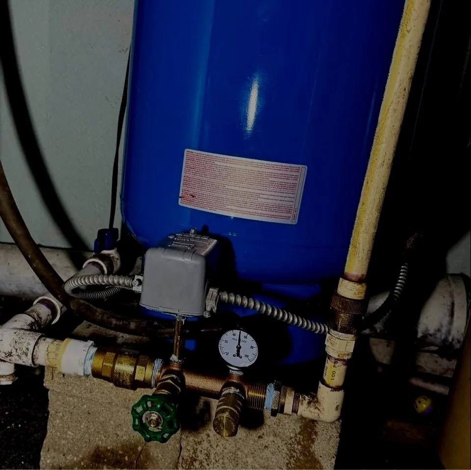 Blue water pressure tank with gauge, valve, and pipes connected underneath.