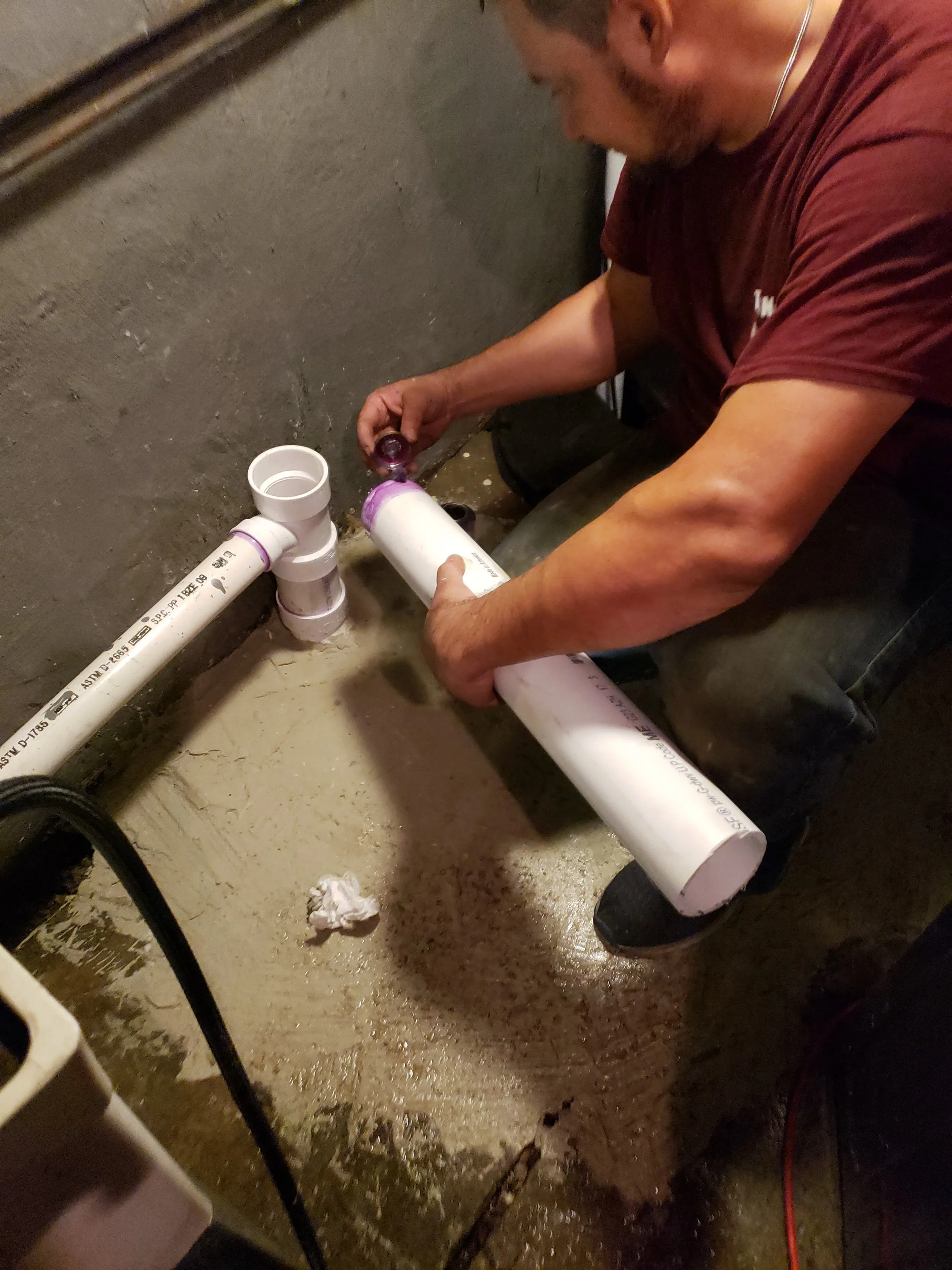 Duran The Plumber LLC installs white PVC pipes under a concrete floor in a building.