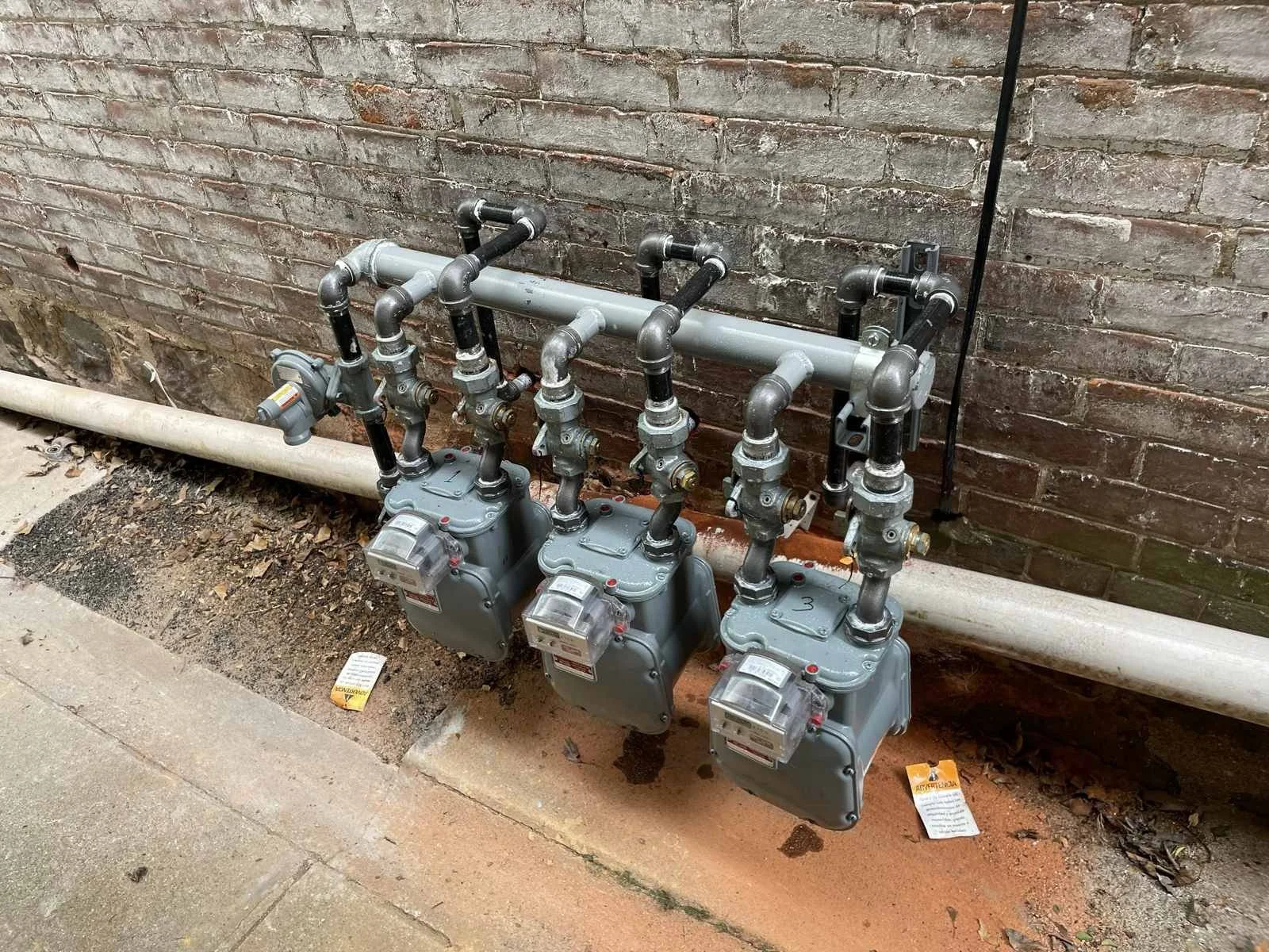 Three gas meters installed outside a brick wall with black and gray piping.