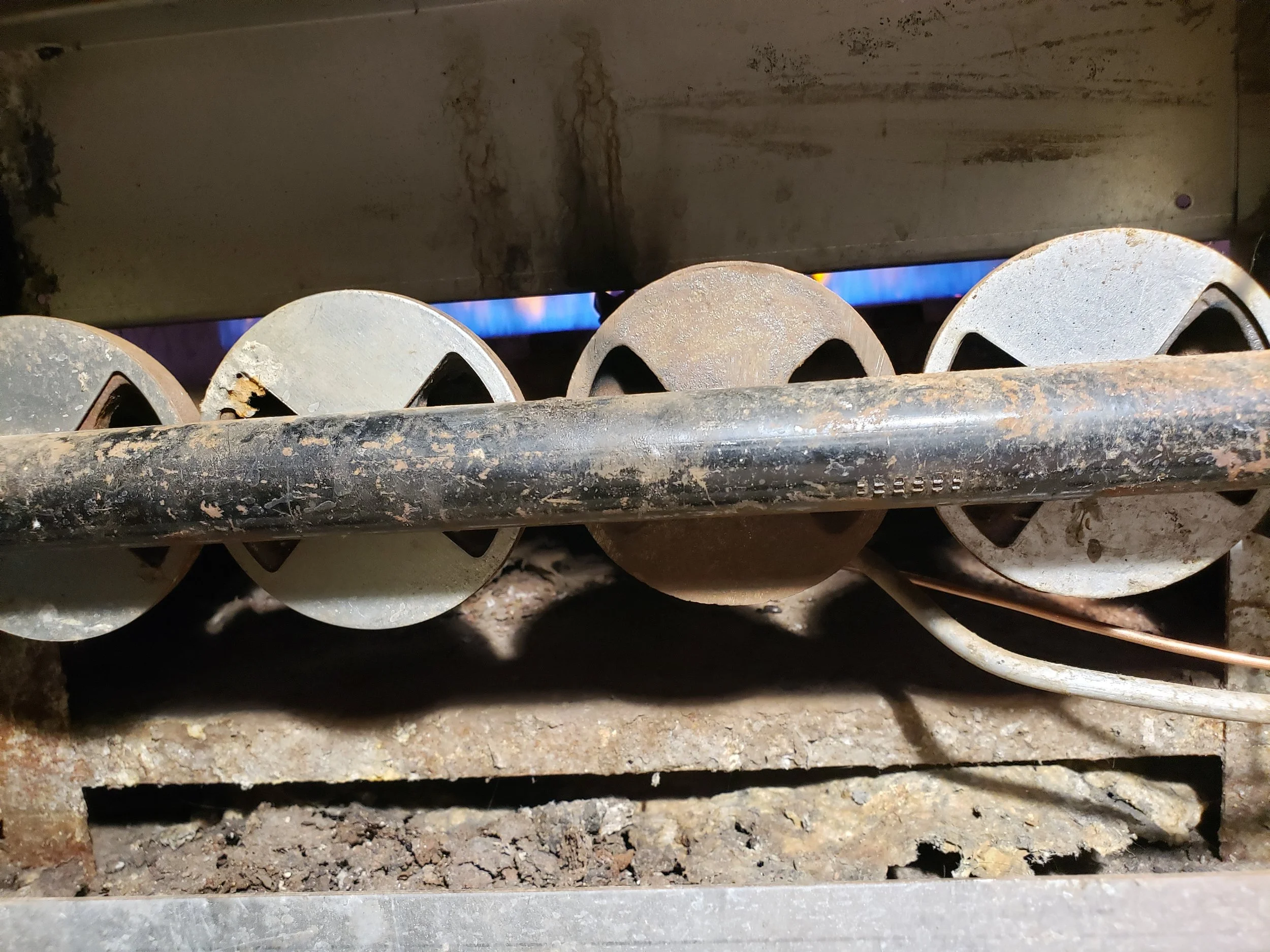Close-up of a dirty stove burner and gas flame underneath, with rust and dirt on the surface.