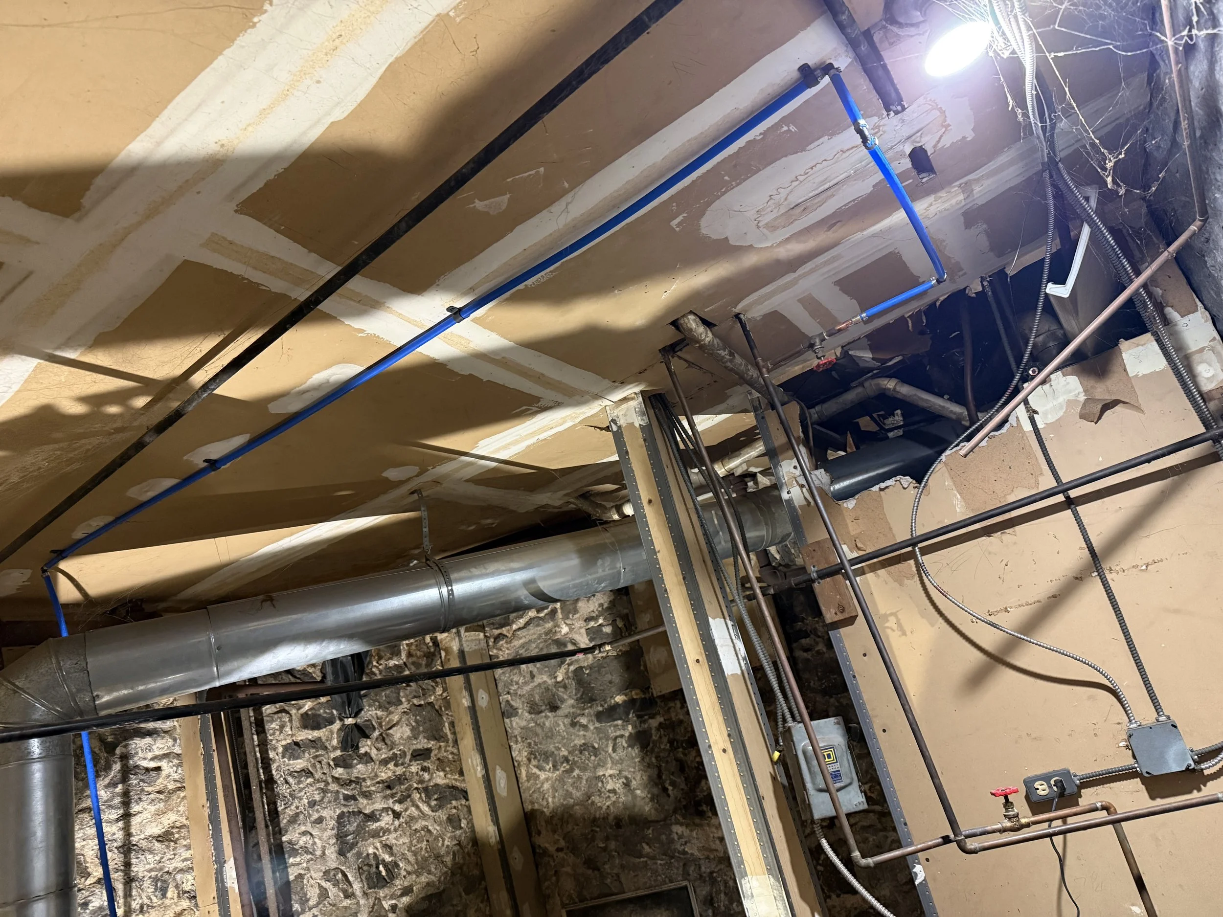 Undeclared construction or plumbing work with exposed pipes, electrical wiring, and unfinished drywall in a building interior.