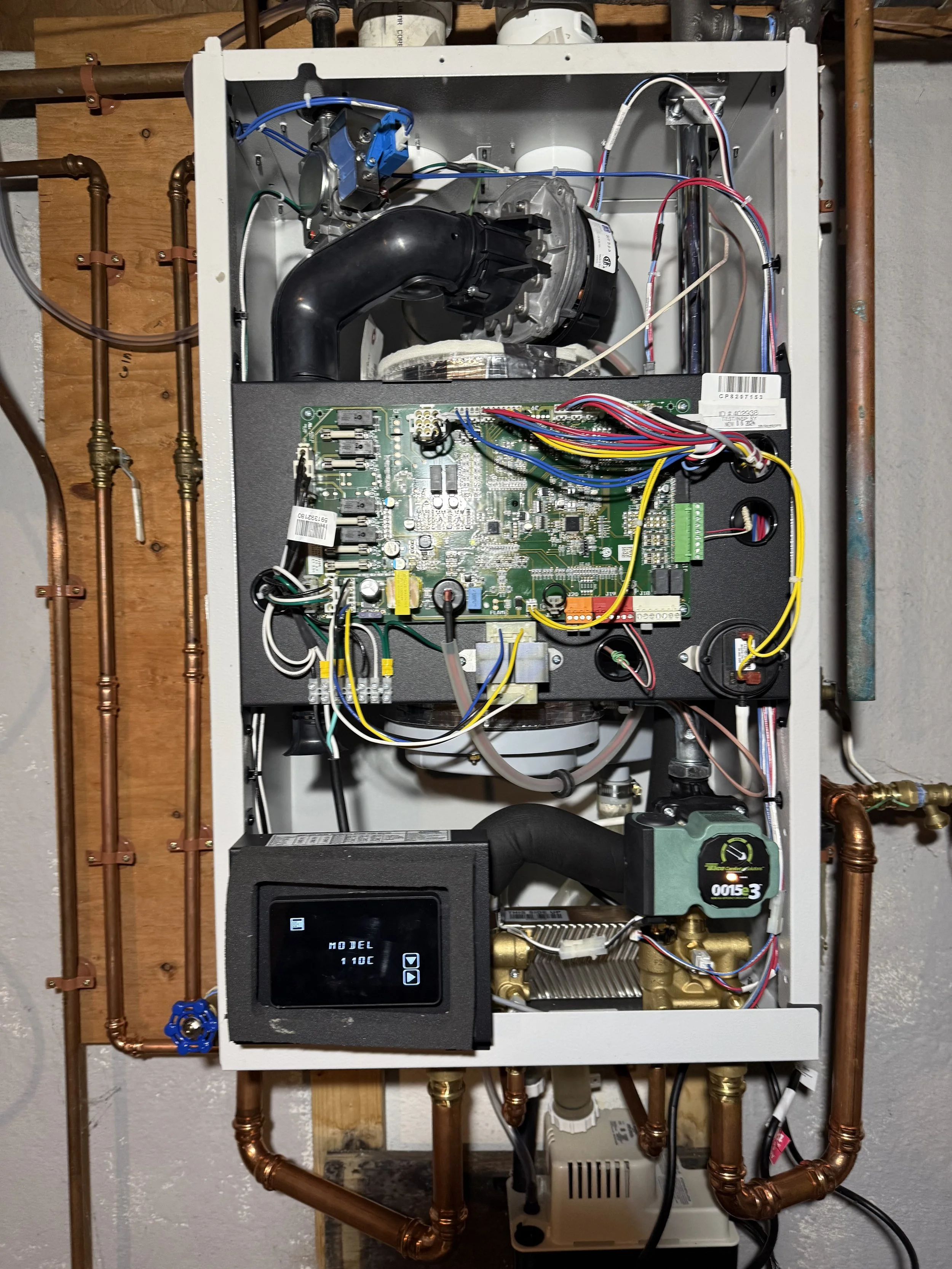 Interior view of a heating or boiler system with copper piping, a circuit board, digital controller, and various mechanical and electrical components.