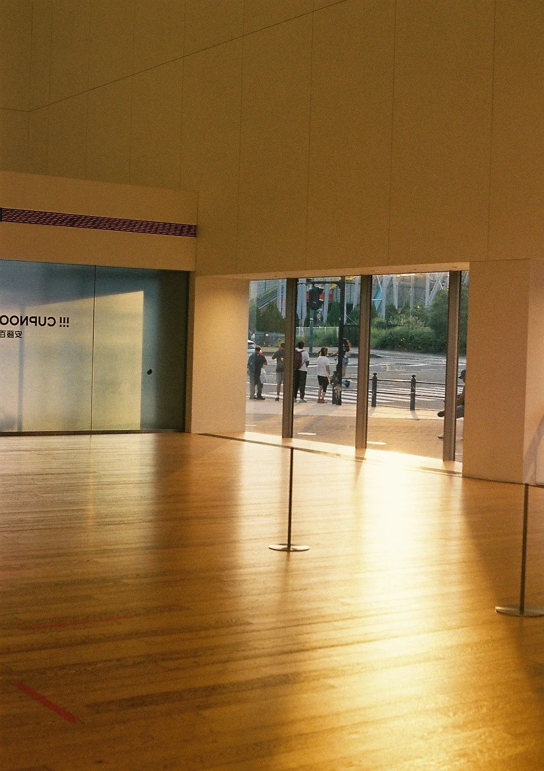 Interior space with wooden flooring, glass sliding doors, and a view of people outside at sunset.