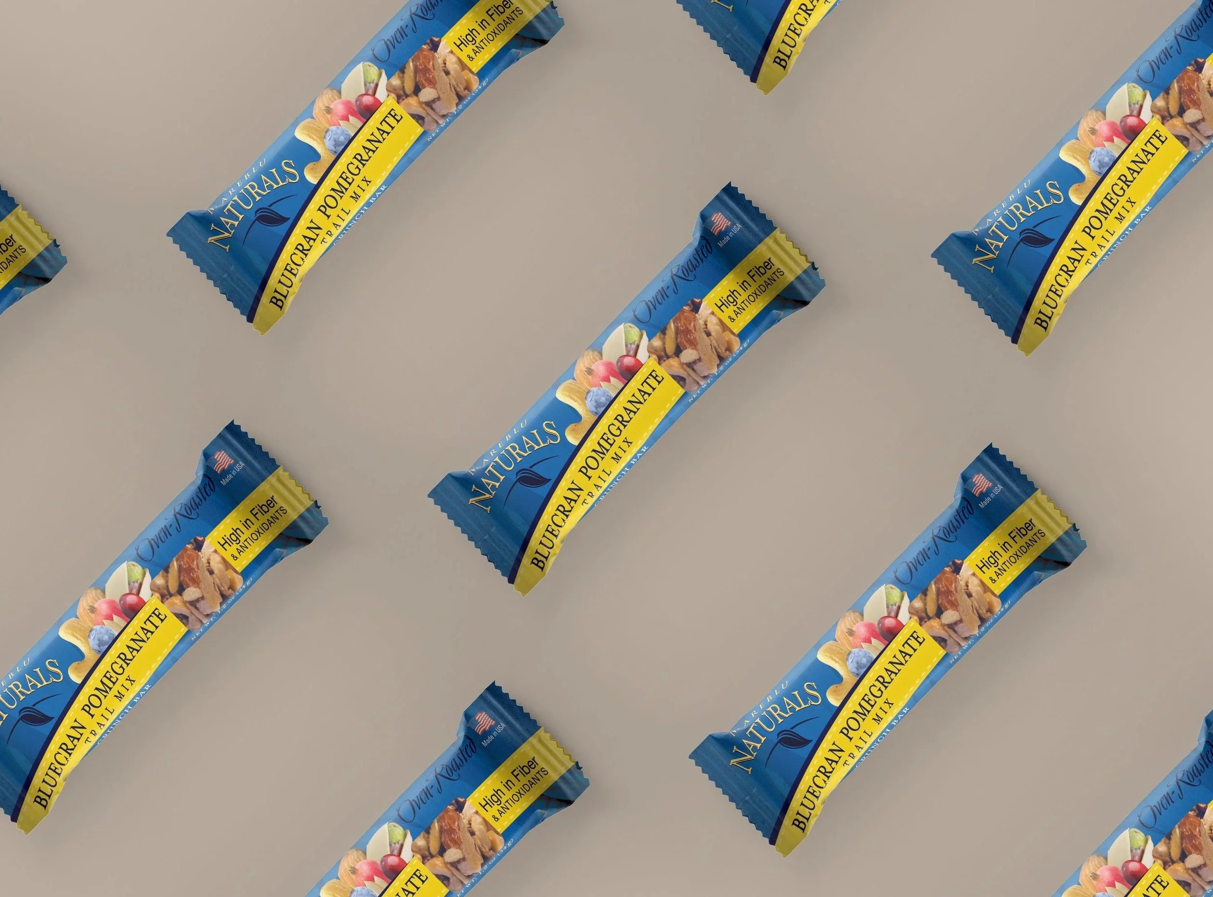 Multiple blue and yellow packaged snack bars labeled 'Blueberry Pomegranate Nutrition Trail Mix' with images of blueberries, pomegranates, and nuts, arranged in a scattered pattern on a white background.