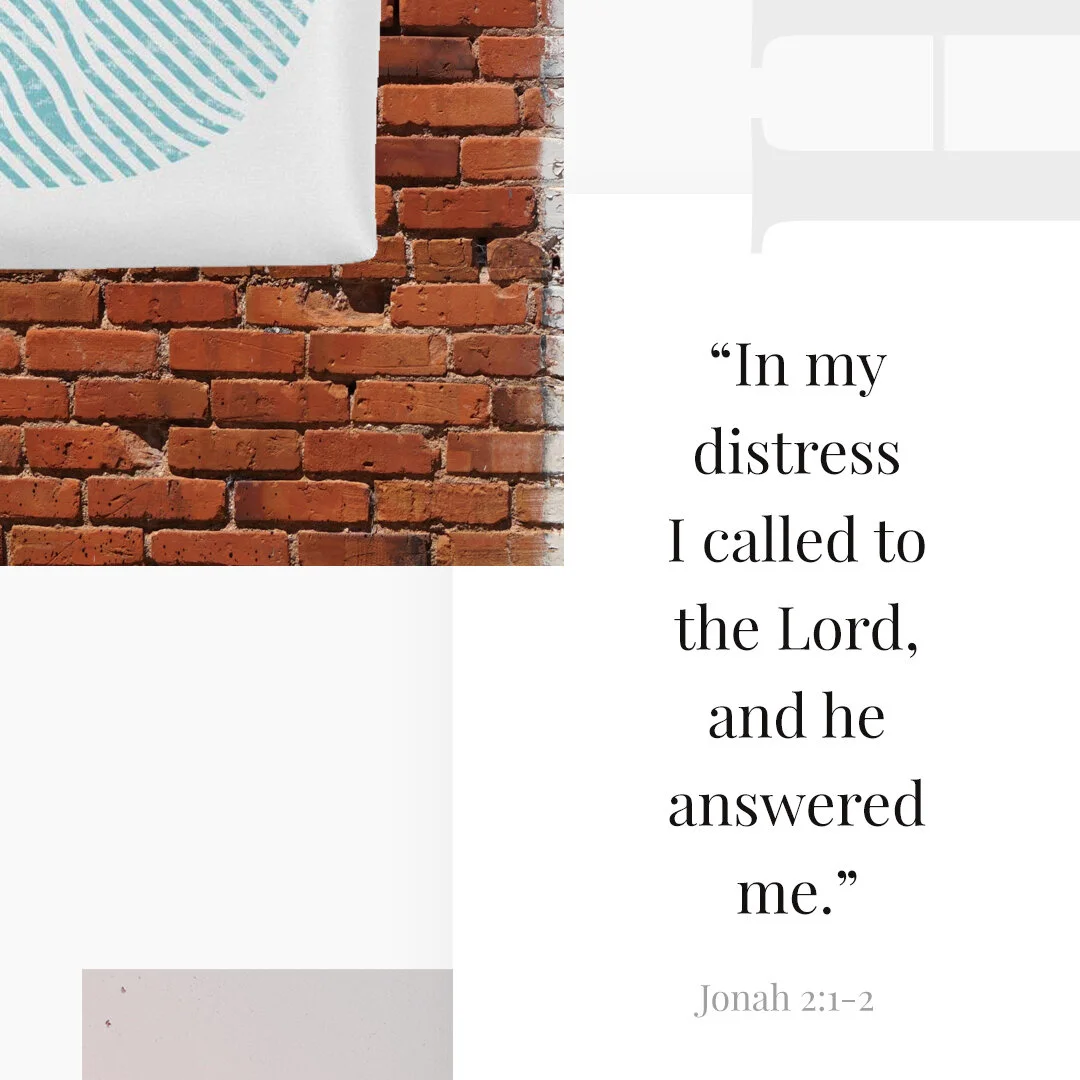 A brick wall with a part of a white canvas displaying a blue circular pattern, and a quote from Jonah 2:1-2 about calling to the Lord in distress.