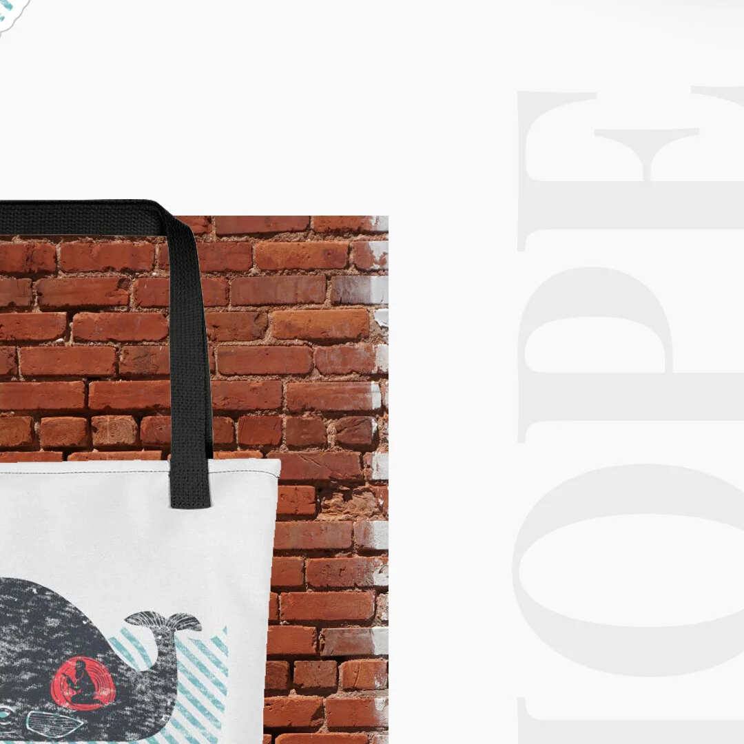 Close-up of a white tote bag with a whale illustration on it, hanging against a brick wall background.