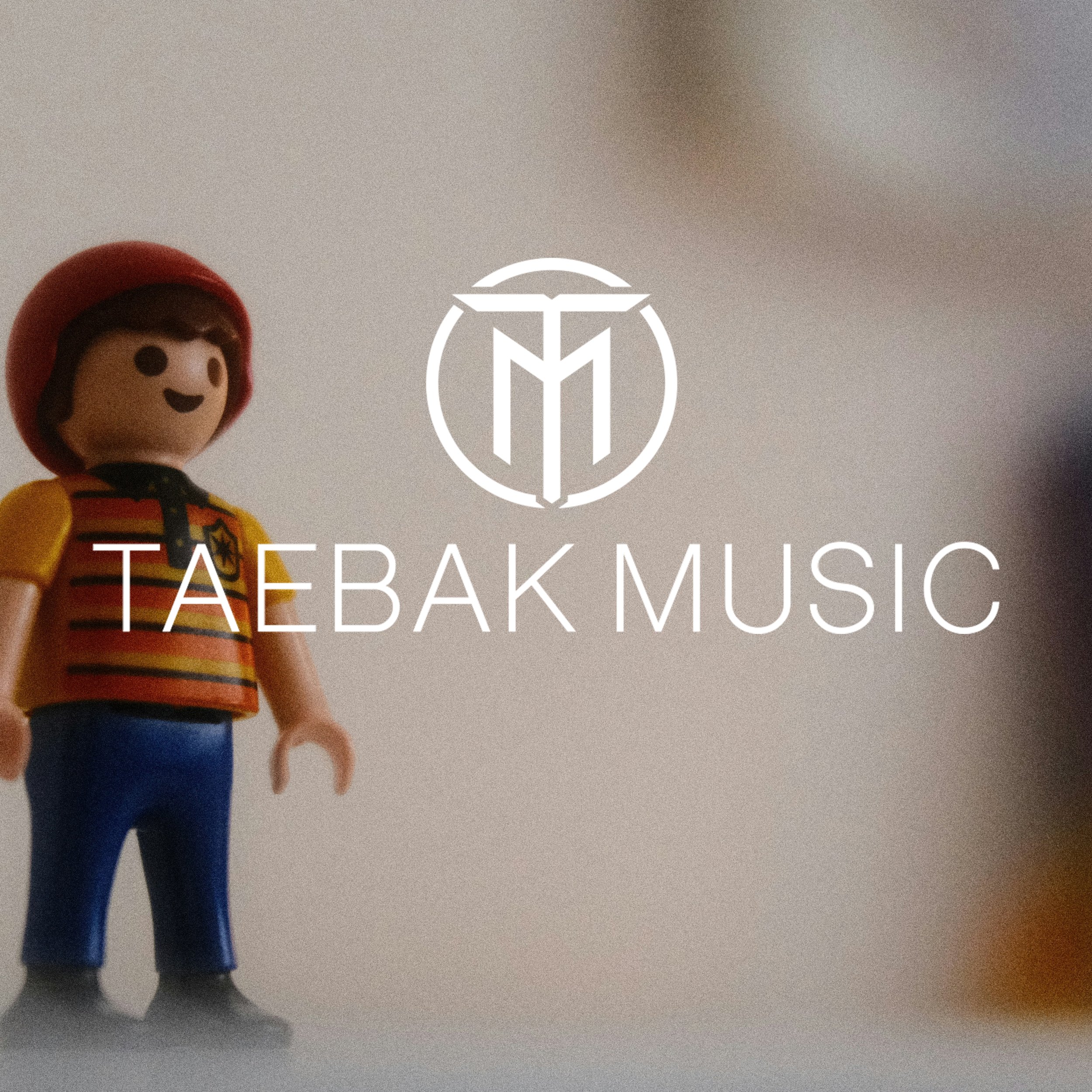 A toy figurine of a person wearing a red hat, yellow and orange striped shirt, and blue pants, standing in front of a light background with the Taebak Music logo overlaid.