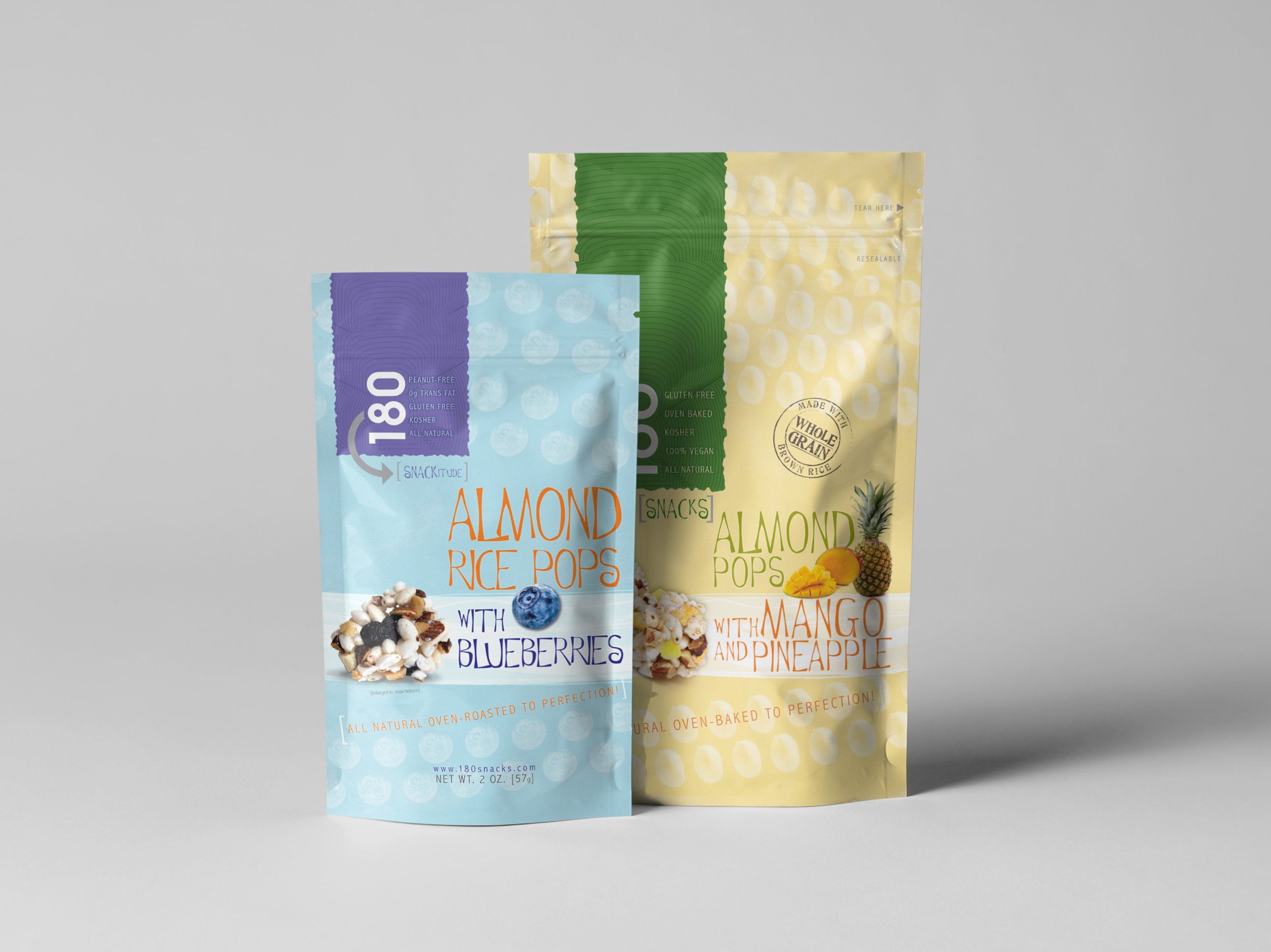 Two bags of almond rice pop snacks, one with blueberries and the other with mango and pineapple, stand against a gray background.