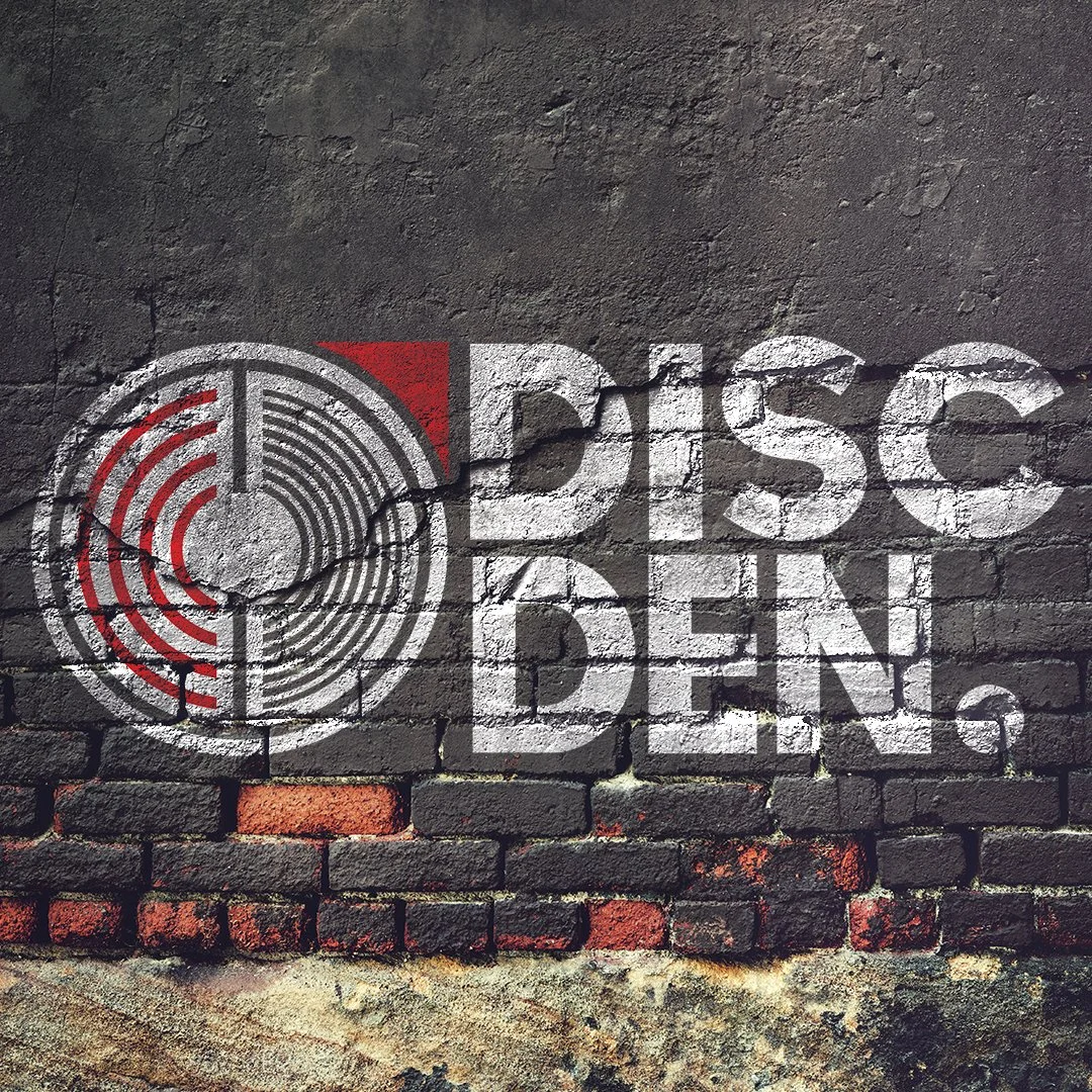Graffiti on a brick wall reading 'DISC DEN' with a circular logo in black, white, and red.