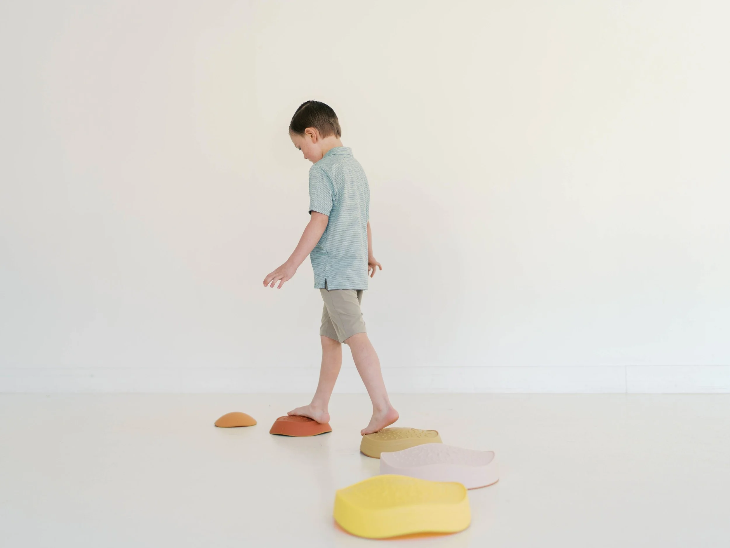 Young boy walking barefoot across colorful stepping stones in a minimalist room as part of physical therapy treatment