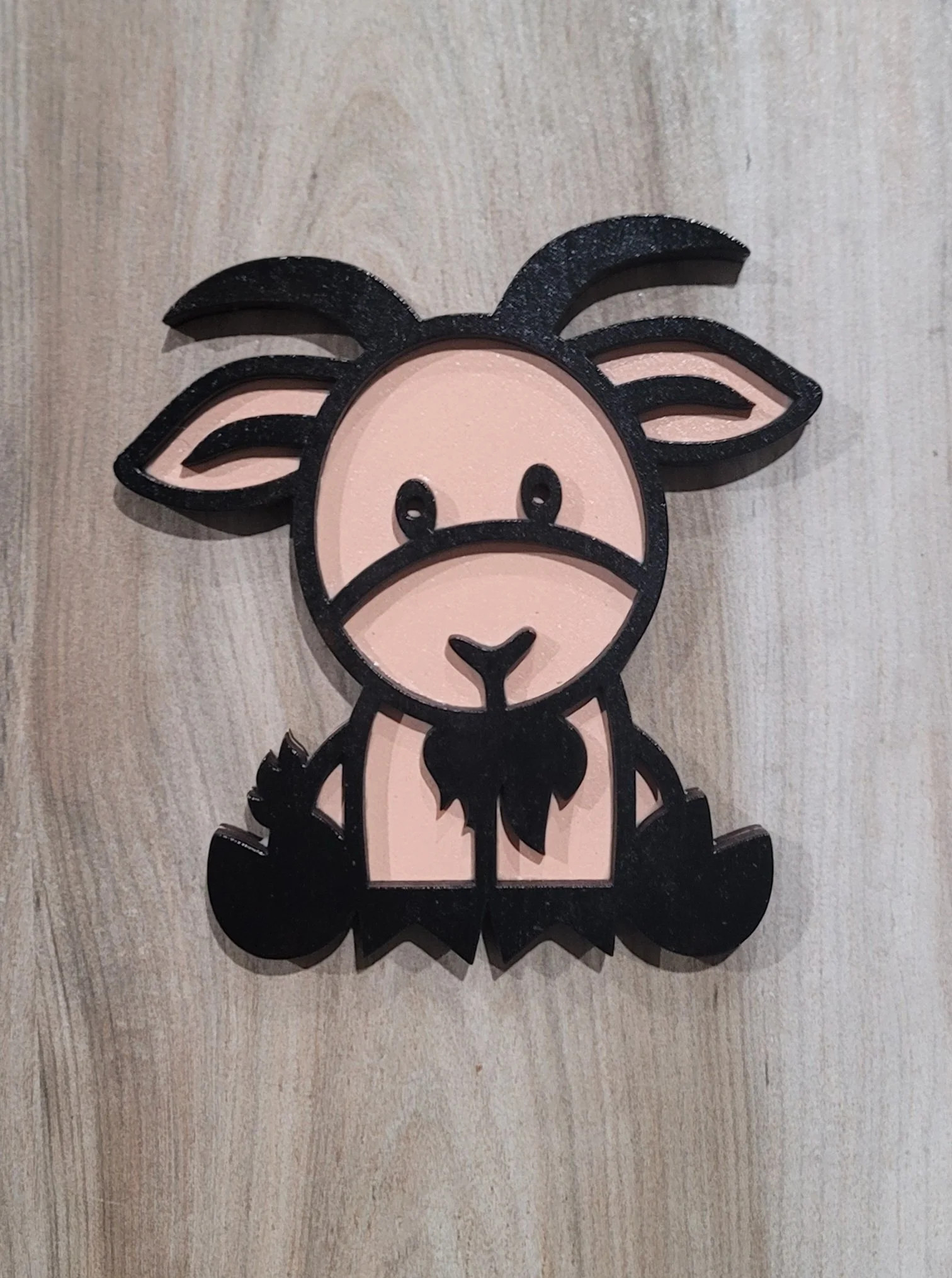 Decorative wall art of a cute cartoon baby goat, with a pink face and black outlines