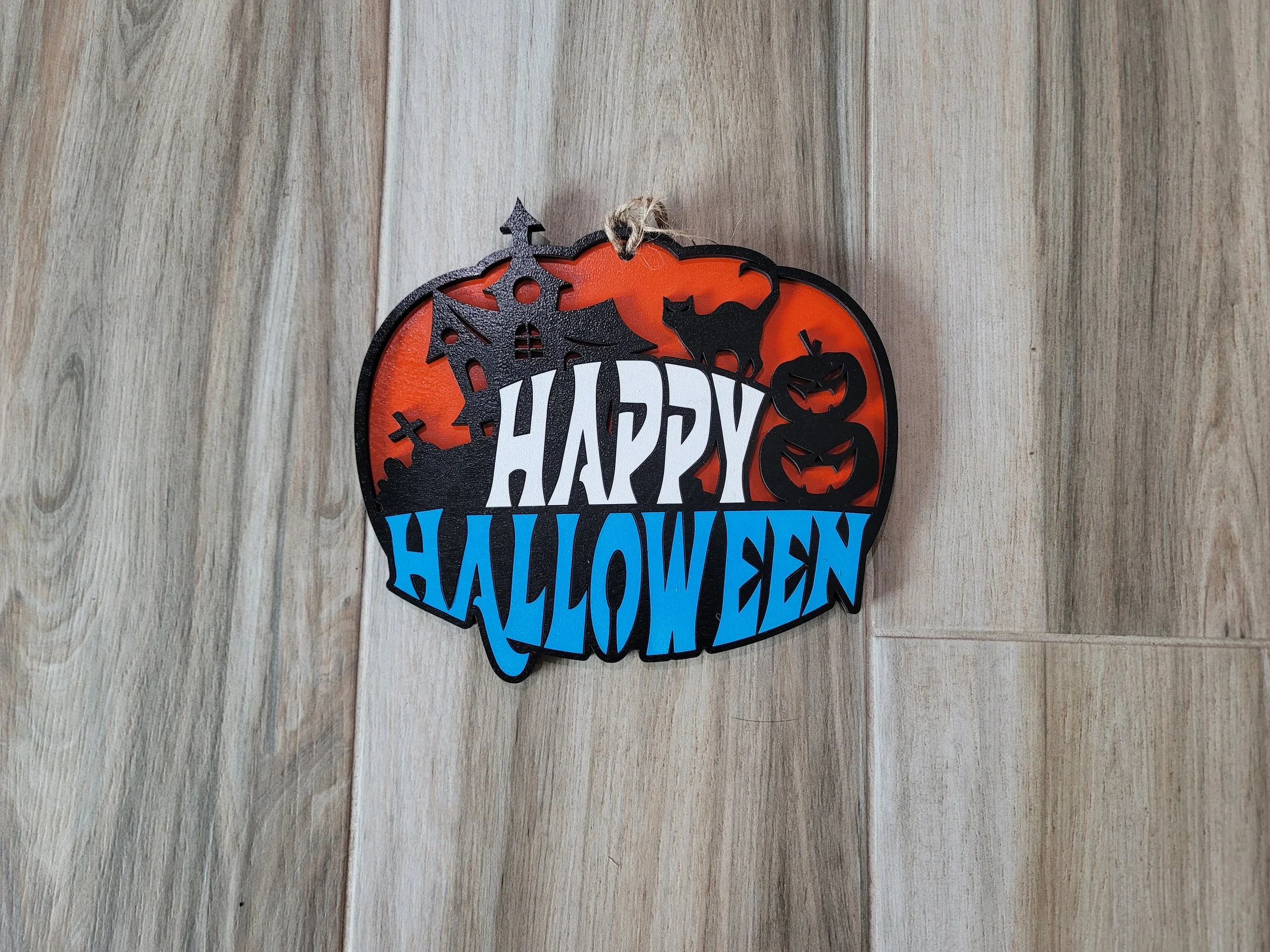 Decorative Halloween sign with a graveyard scene, black cat, pumpkins, and the words 'Happy Halloween' in white and blue lettering.