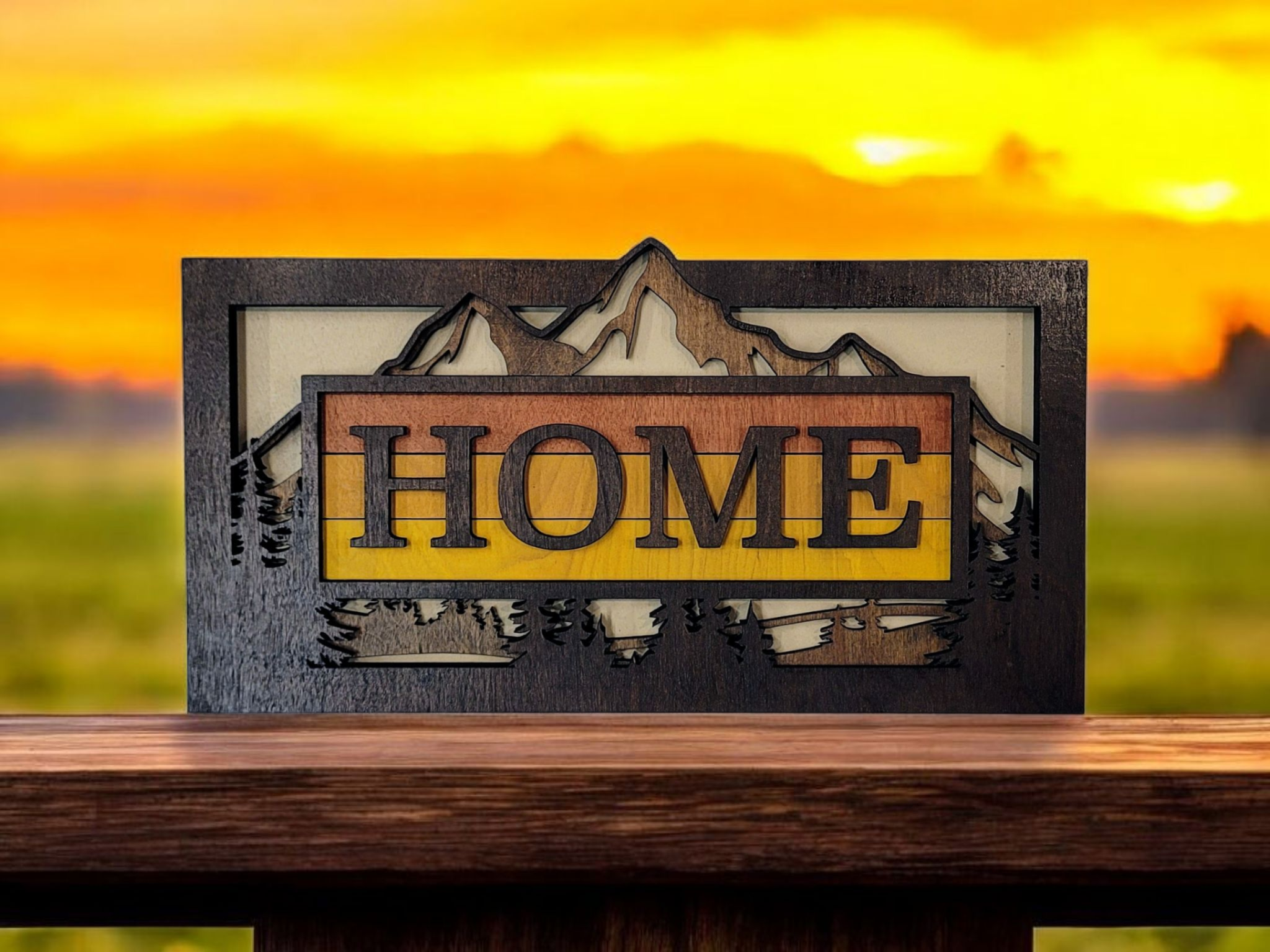 Wooden decorative sign with mountains and trees in the background that spells out 'HOME', with a sunset sky.