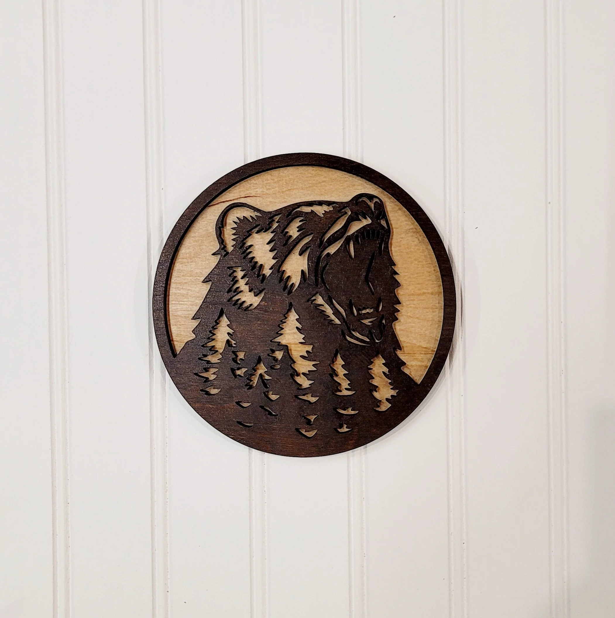 Wooden circular wall art featuring a carved bear head and pine trees.