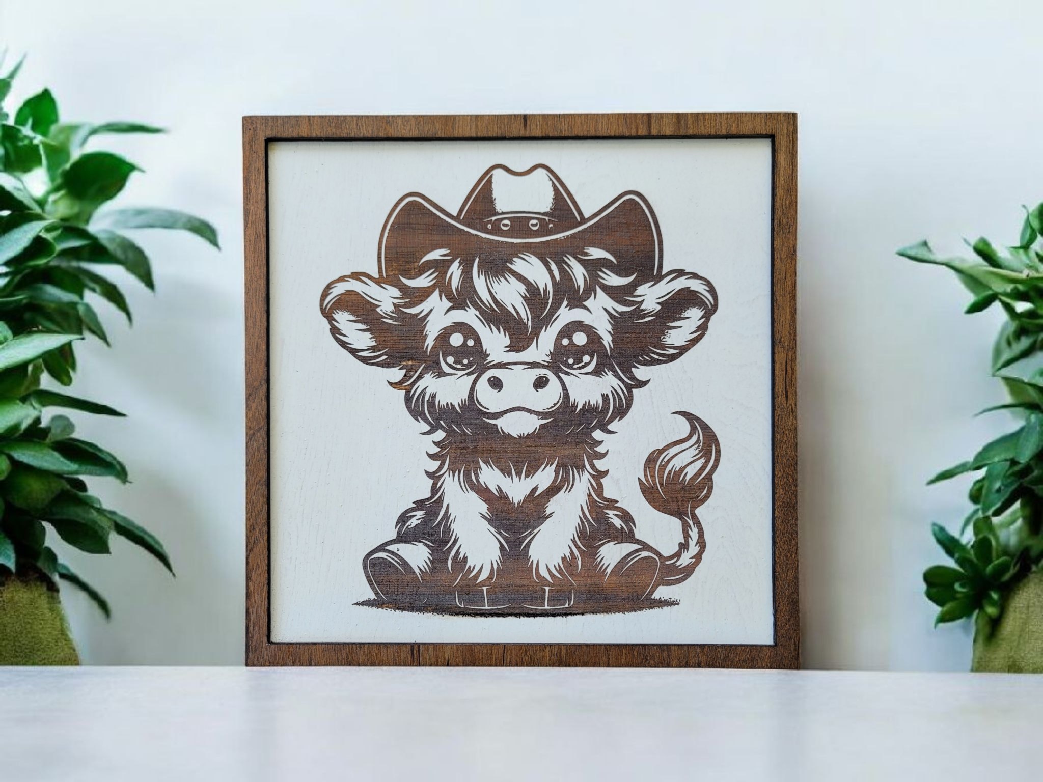 Illustration of a cute puppy with large eyes wearing a cowboy hat, framed and displayed with green plants on either side.