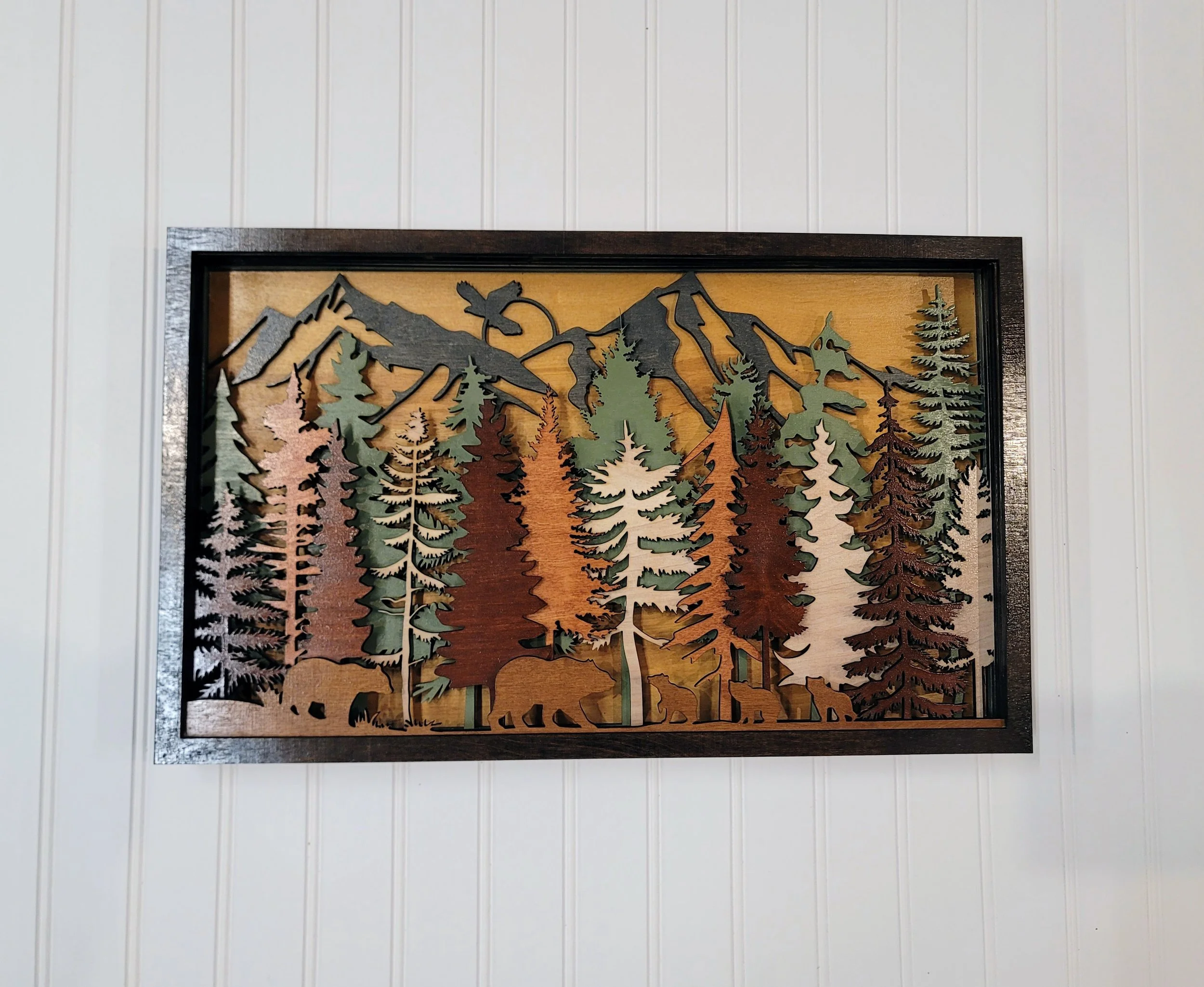 Wooden wall art depicting mountain scenery, pine trees, and bears, framed by a dark wooden border.